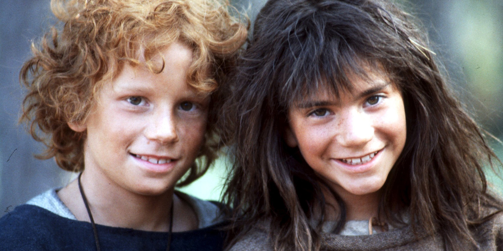 Ett foto på två barn, en pojke med rödlockigt hår och en flicka med mörkt rufsigt hår som ler.