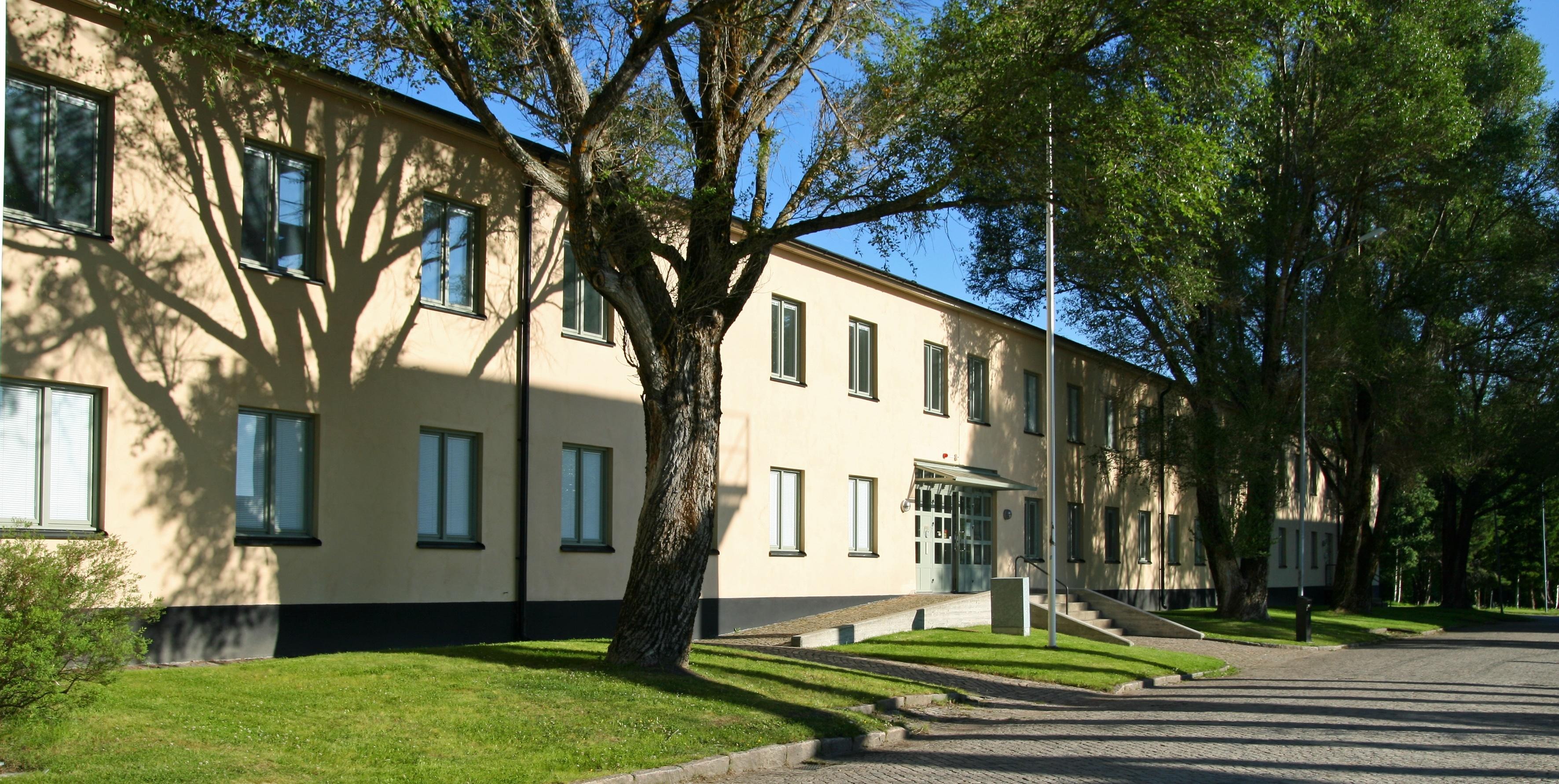 A white house in two storeys with tress in the front.