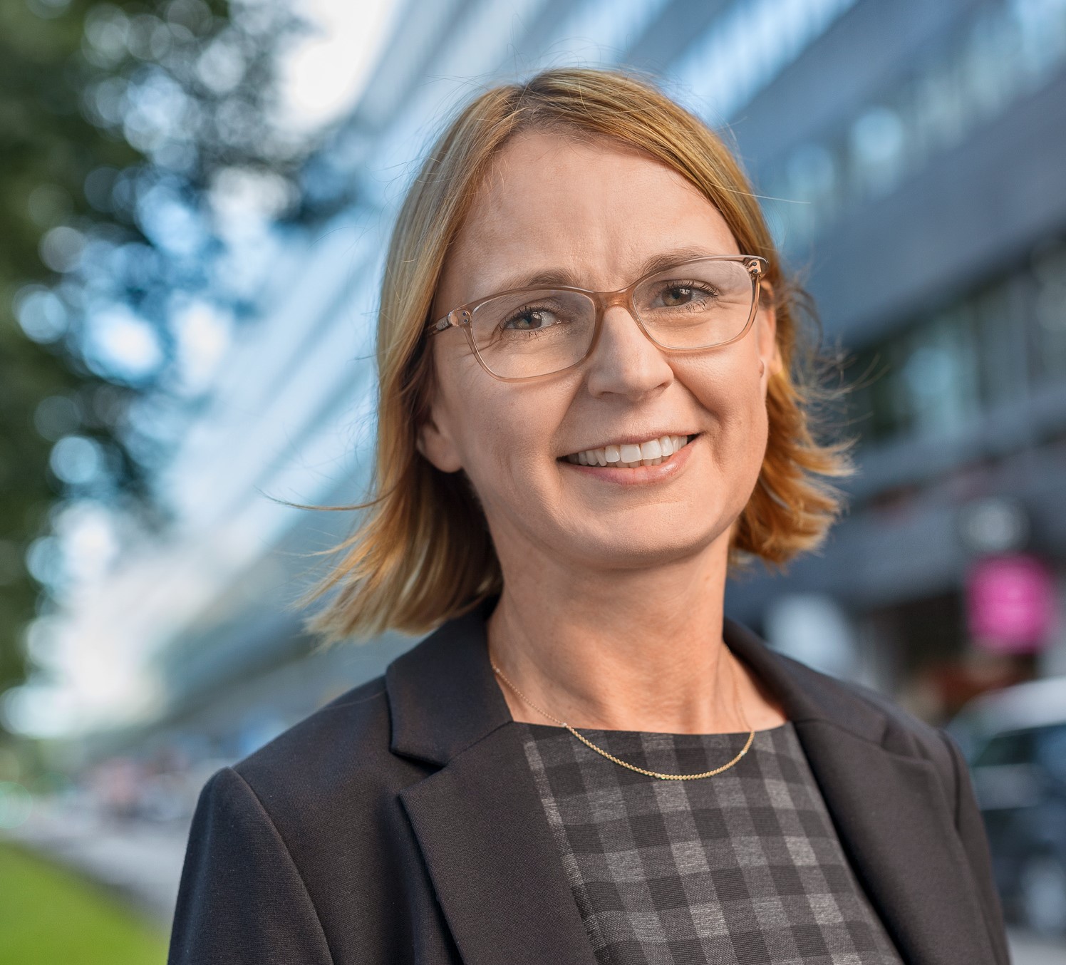 Portträttbild av riksbibliotekarie Karin Grönvall. Hon har haklångt hår, glasögon, en grårutig tröja och en grå kavaj. Bilden är tagen utomhus.