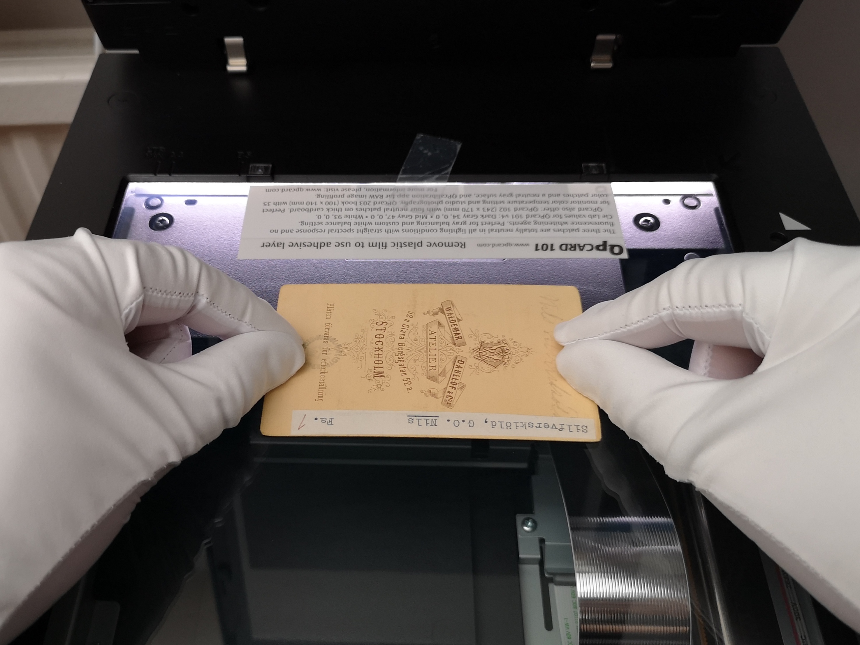 Ett visitkortsporträtt placerat på en skanner av ett par händer iklädda vita handskar.