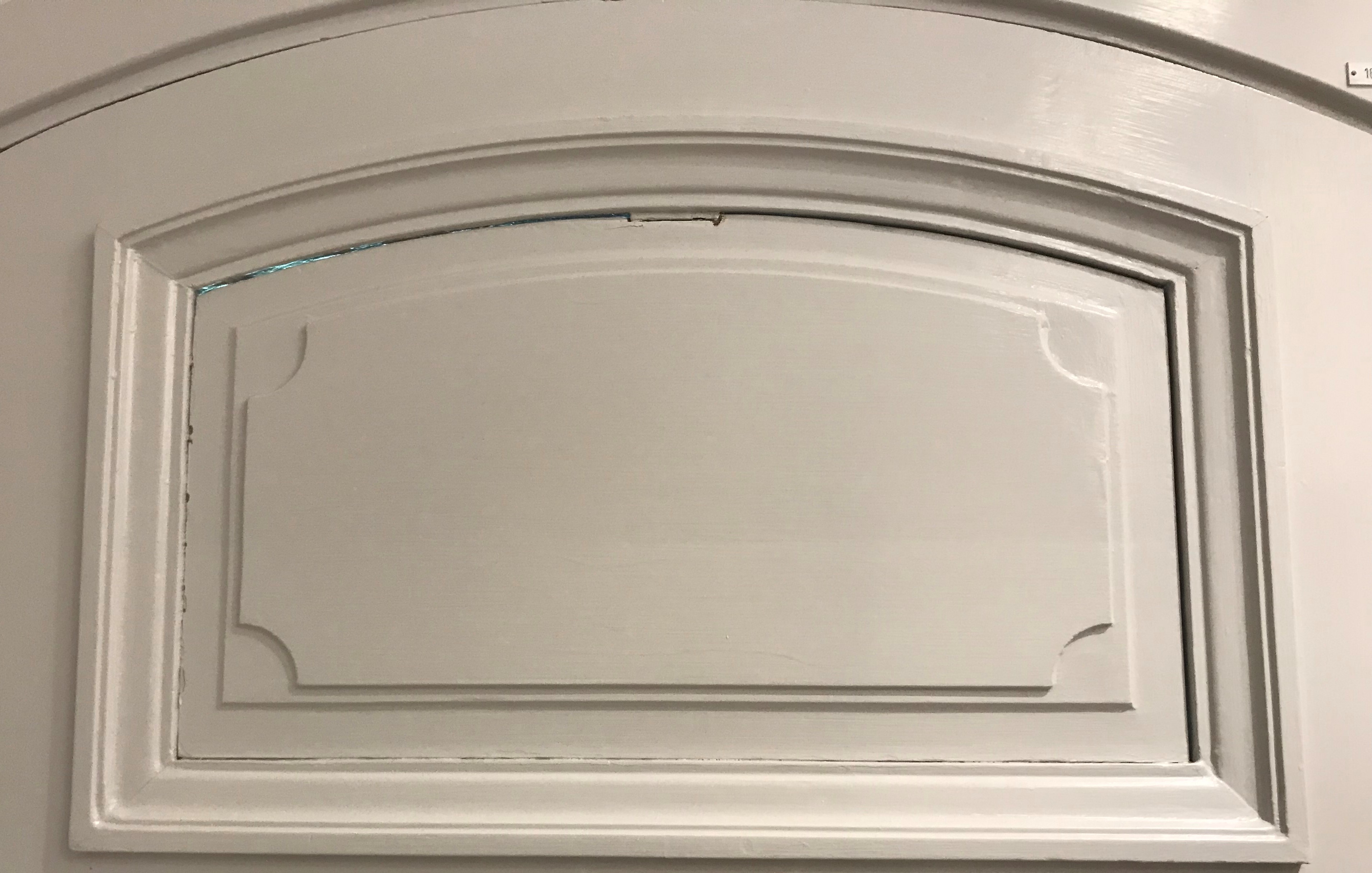 Fotografi föreställande övre halvan av en dörr målad i ljusgrått, med en stängd lucka.