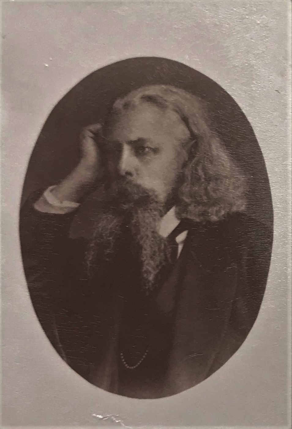 Svartvitt fotografi av en man med långt grått hår och långt tudelat skägg som lutar huvudet mot höger hand.
