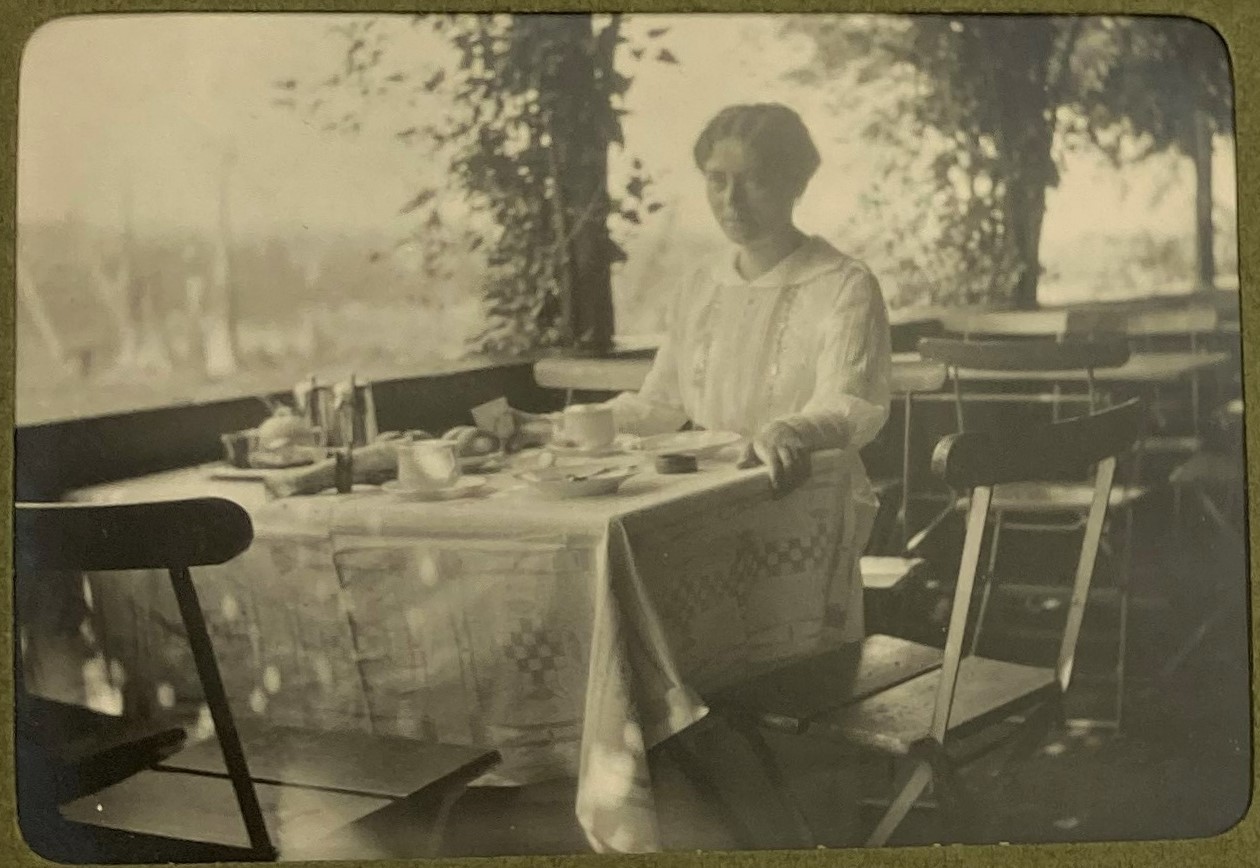 Svartvitt fotografi av en kvinna som sitter vid ett dukat bord på en terrass.