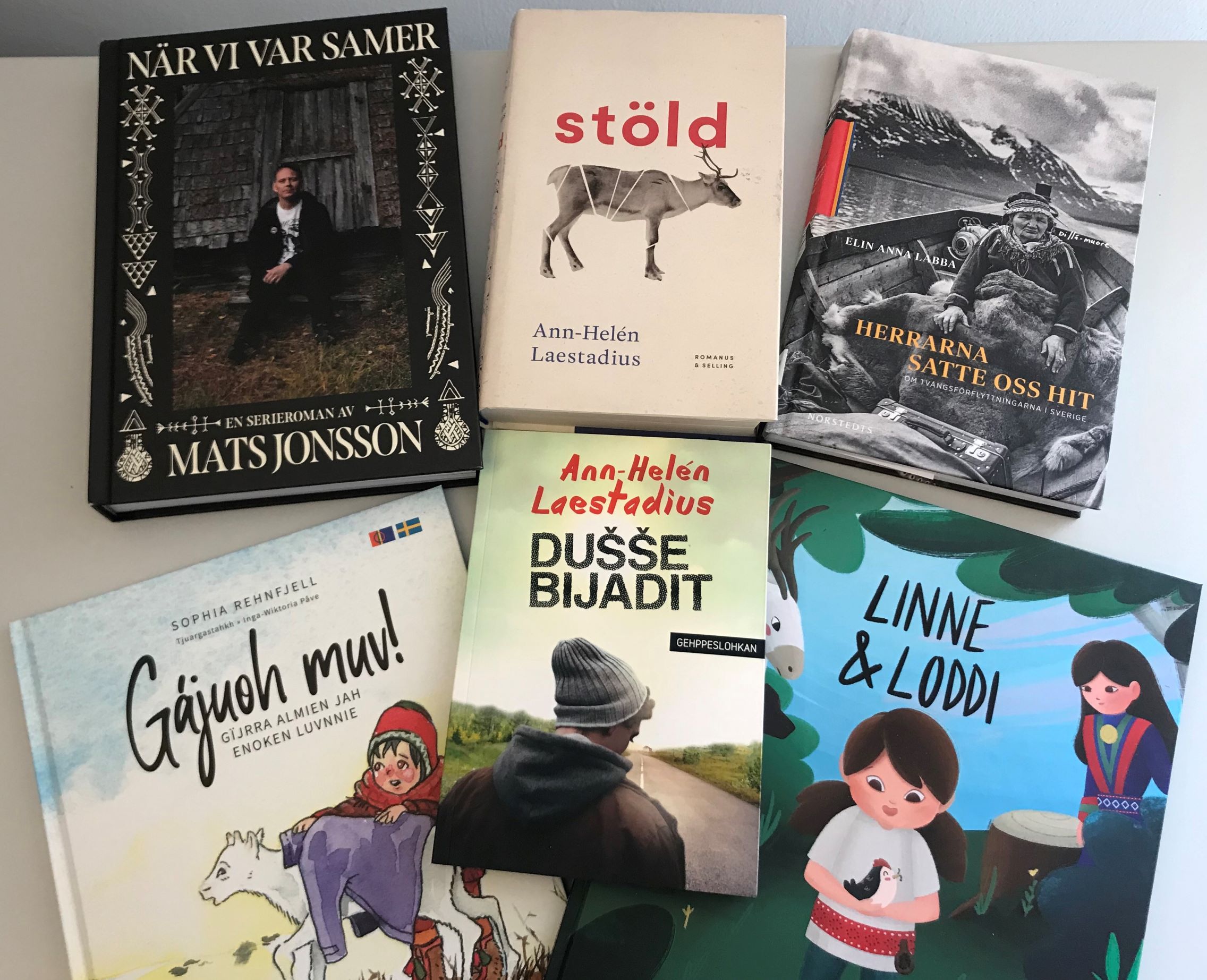 Sex böcker liggande på ett bord, samtliga har omslag eller titlar som syftar på samisk kultur eller historia.