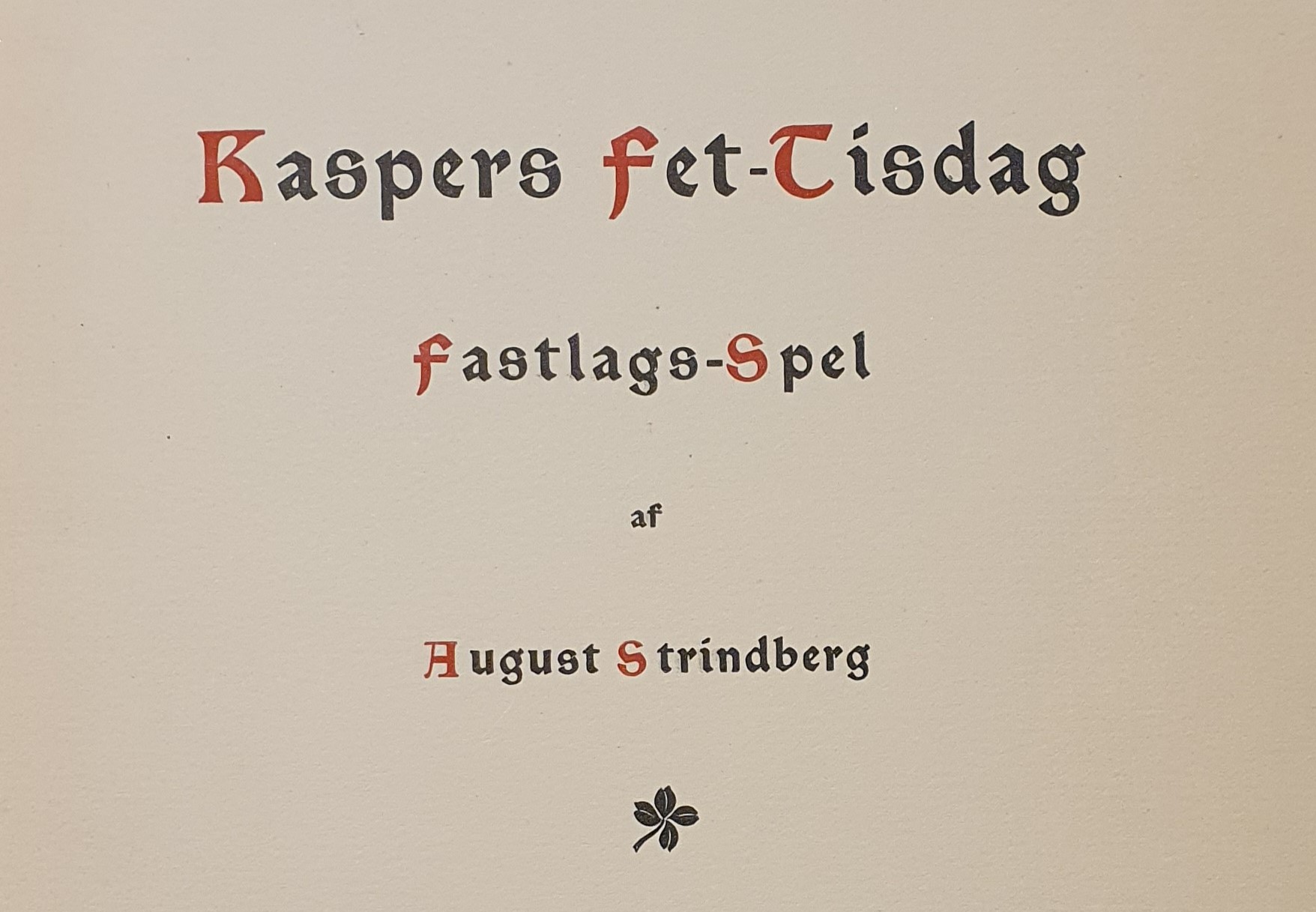 Tryckt titel i tre rader på vitt papper, med röda inledande bokstäver i varje ord eller namn. Under titeln en stiliserade fyrklöver i svart.