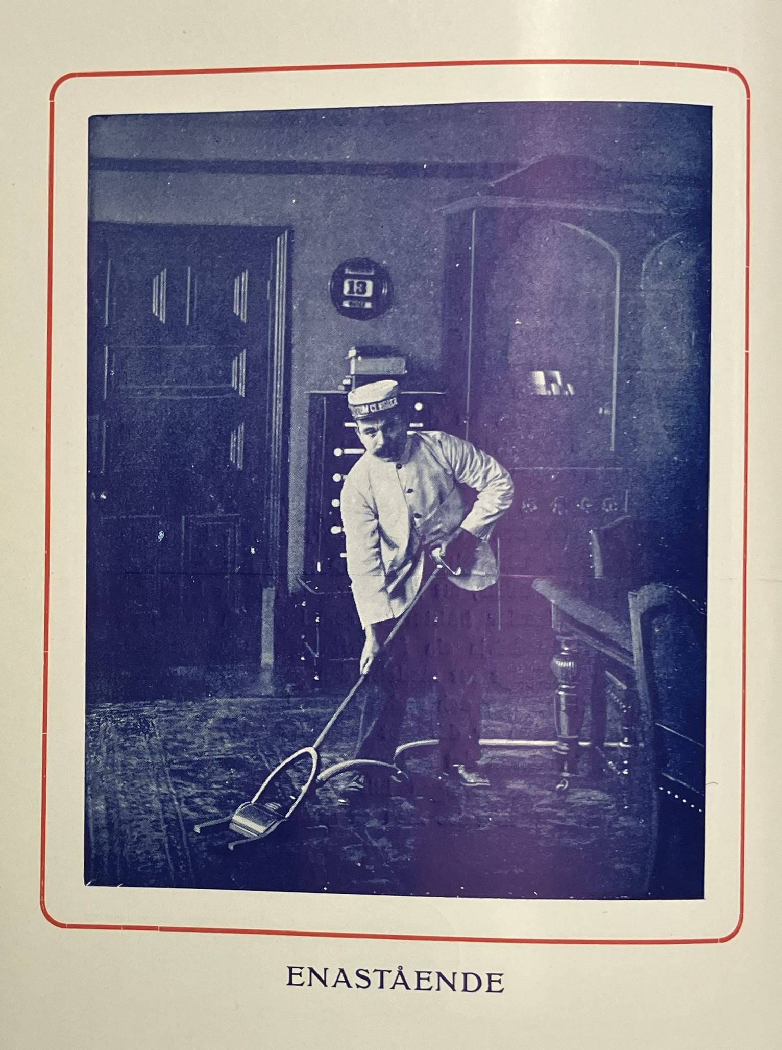 En uniformklädd man poserande medan han dammsuger en matta i en hemmamiljö.