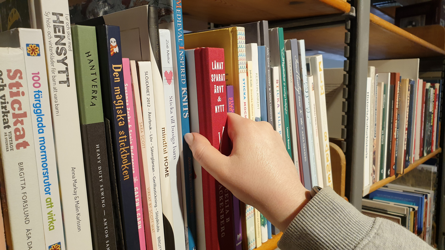 En hand tar ut en bok från en bokhylla