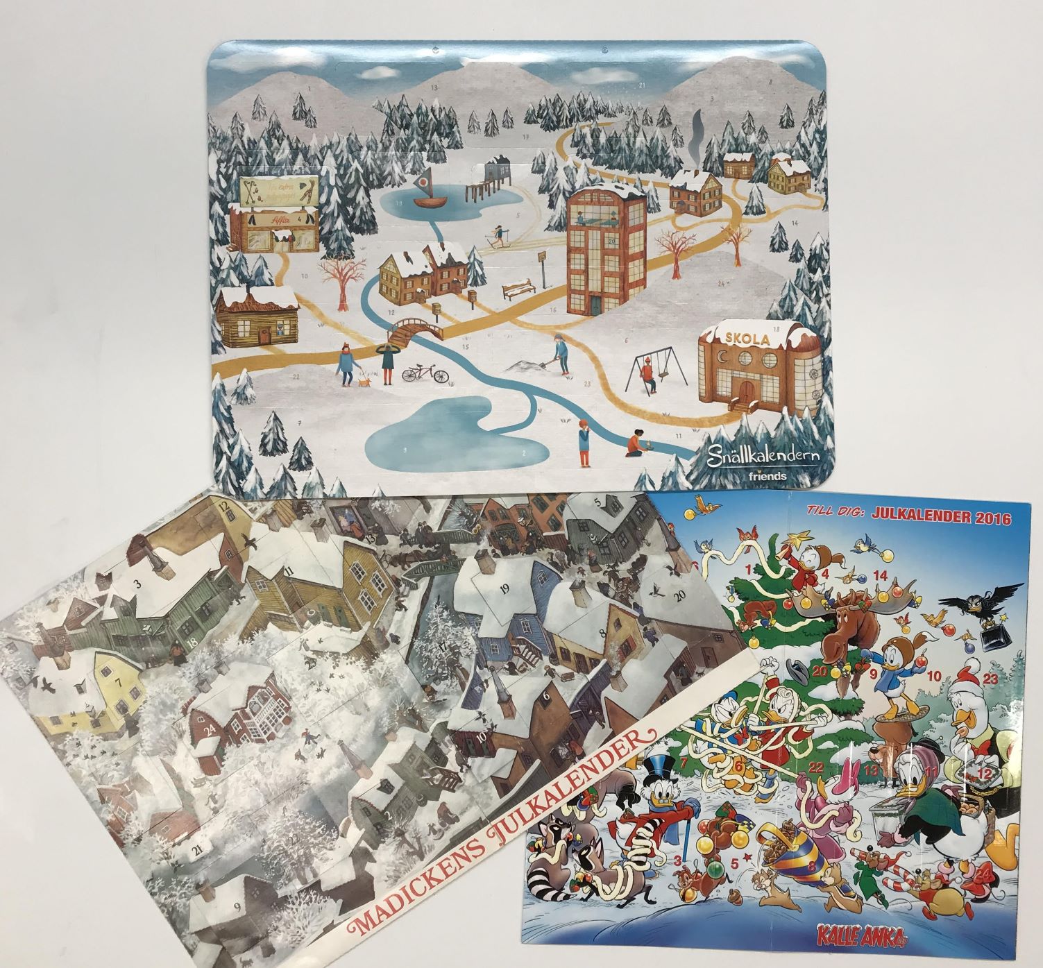 Överst Snällkalendern med vintermotiv över en stad, till vänster Madickens julkalender och till höger en kalender där Kalle Anka & co förbereder julen