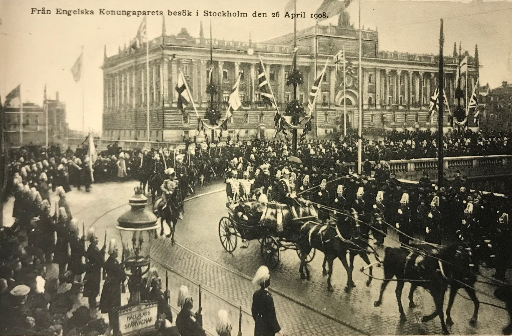 Svartvitt vykort som visar en procession med vagnar framför Stockholms slott, som är omgivet av folkmassor och flaggor.