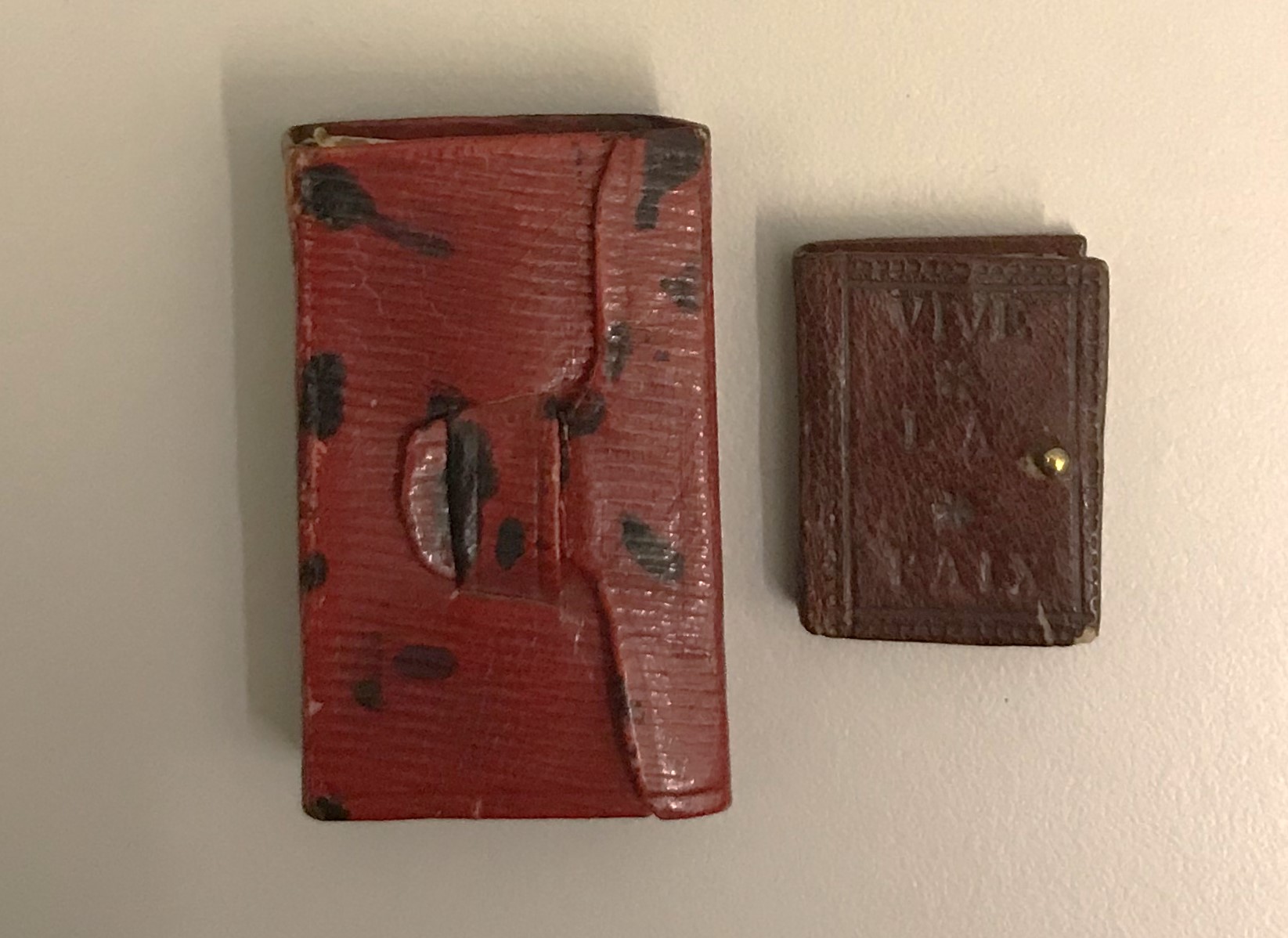 Färgfoto av en väldigt liten bok i brunt skinnband bredvid ett något större rött läderetui.