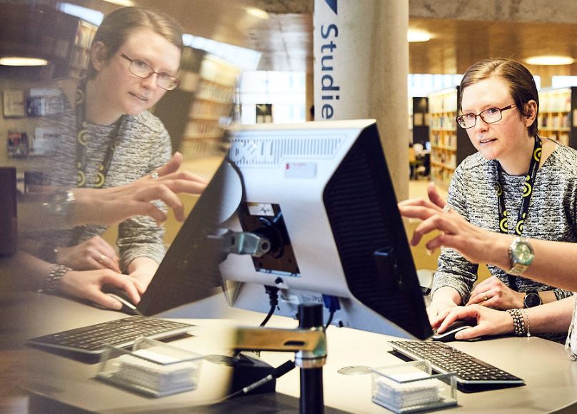 Person framför en dator i biblioteksmiljö.