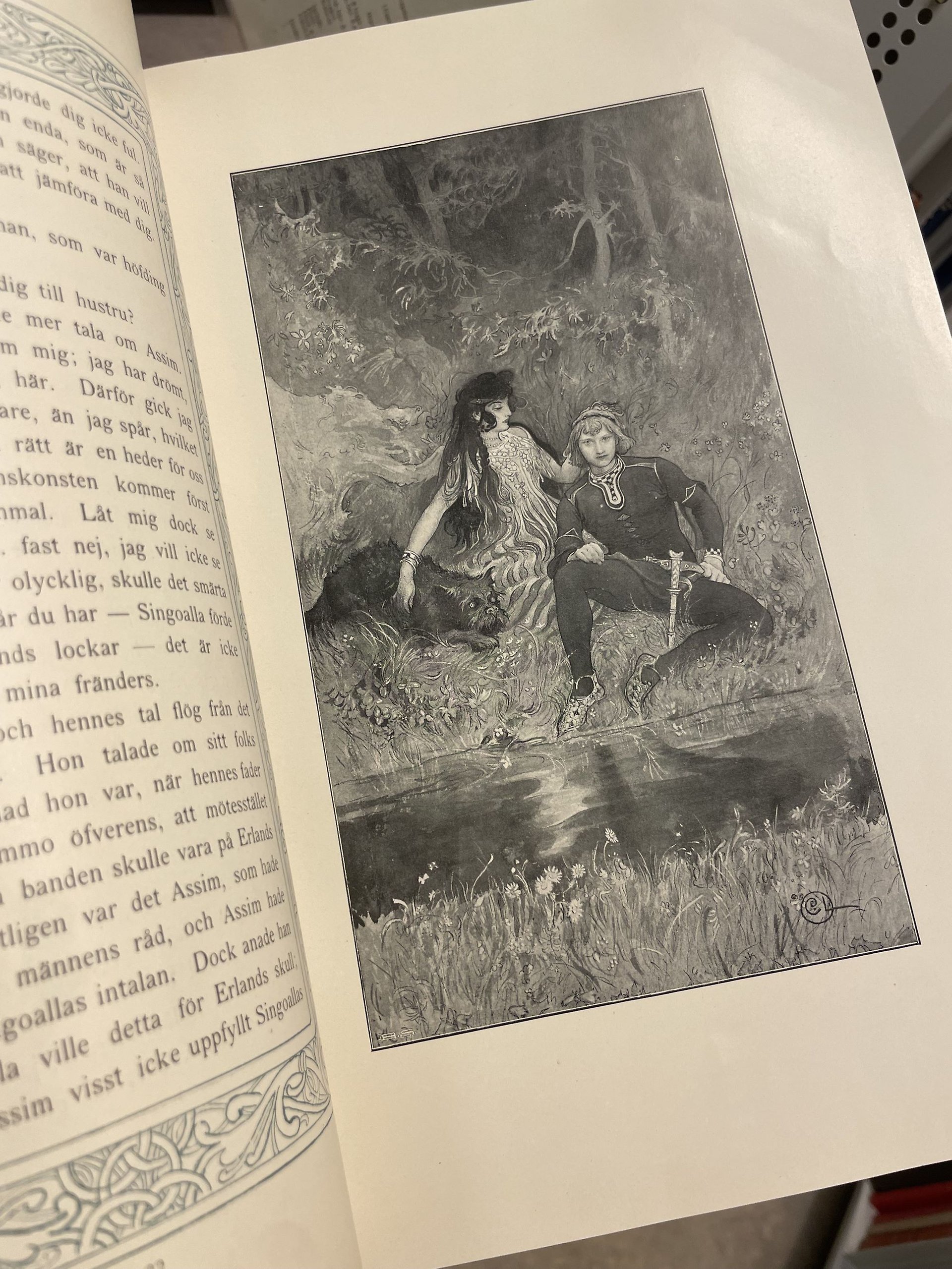 Färgfoto av en uppslagen bok med en svartvit illustration föreställande en vacker mörkhårig kvinna som sitter vid ett vattendrag tillsammans med en stor hund och en ung man klädd i medeltida kläder.