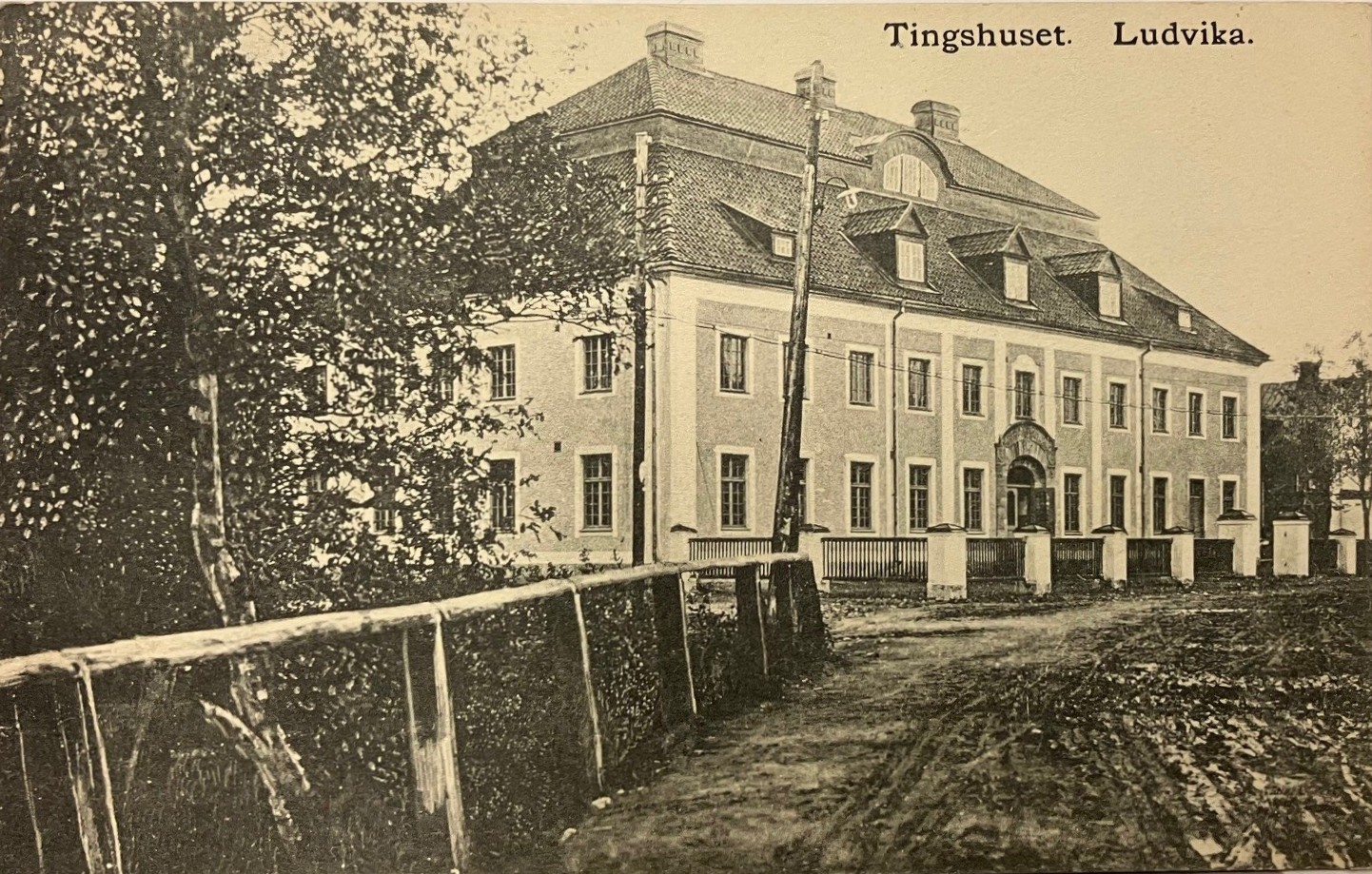 Svartvitt vykort med väg som leder fram till ett pampigt hus med brutet tak.