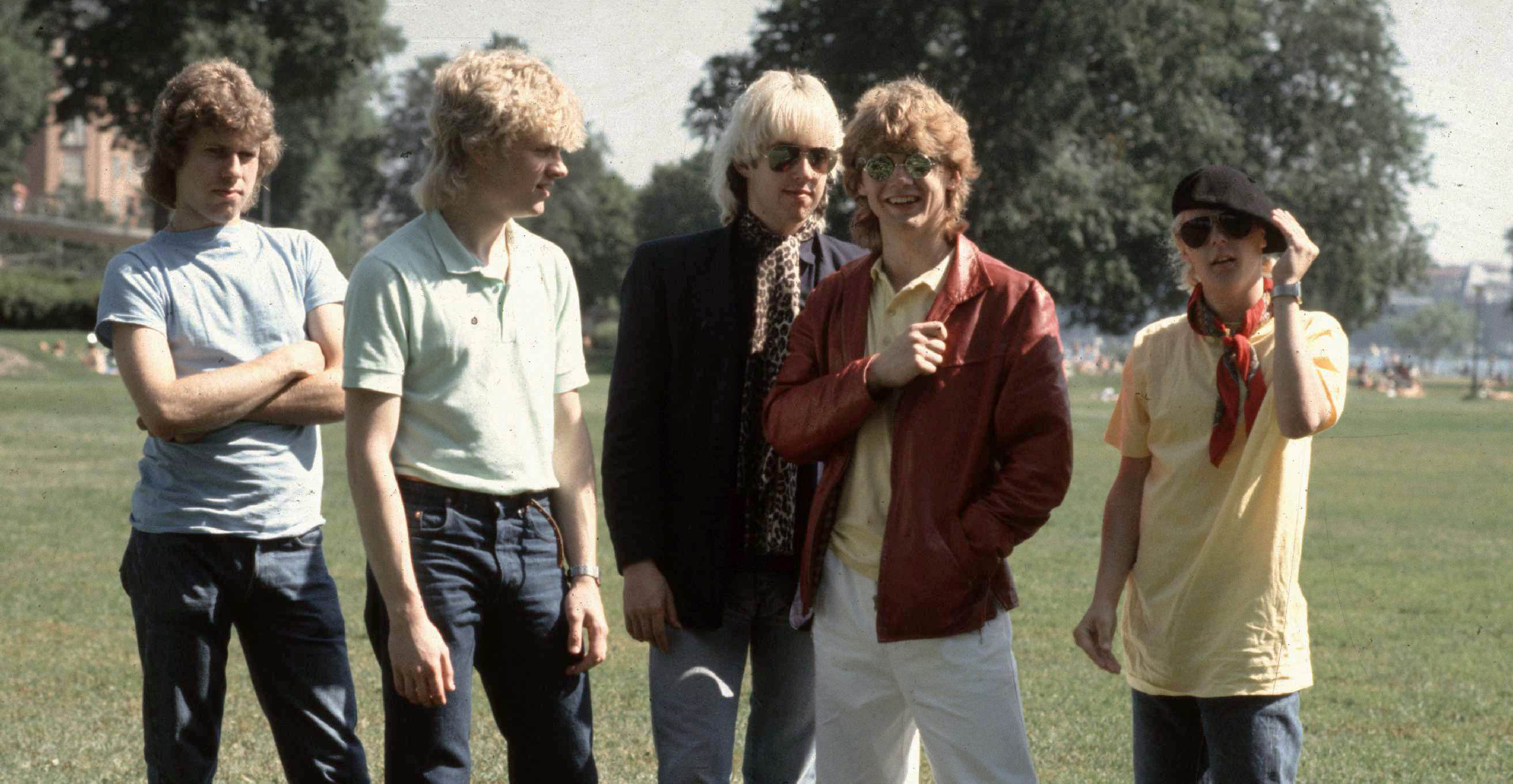 Bilden visar 5 unga killar i en park. Alla med typiska 80-talsfrisyrer.
