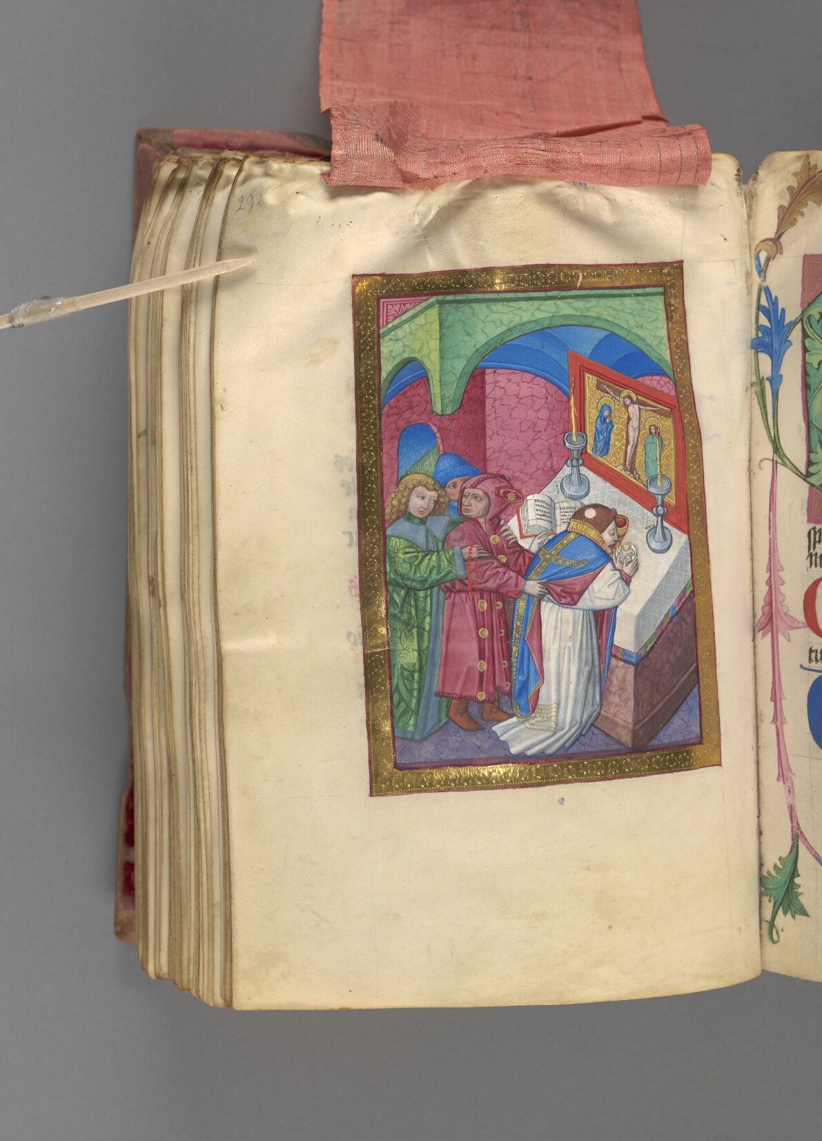 Färgfoto av uppslagen bok med bild i guldfärgad ram som föreställer en person som böjer sig framför ett altare. Bredvid står bland annat en narr.