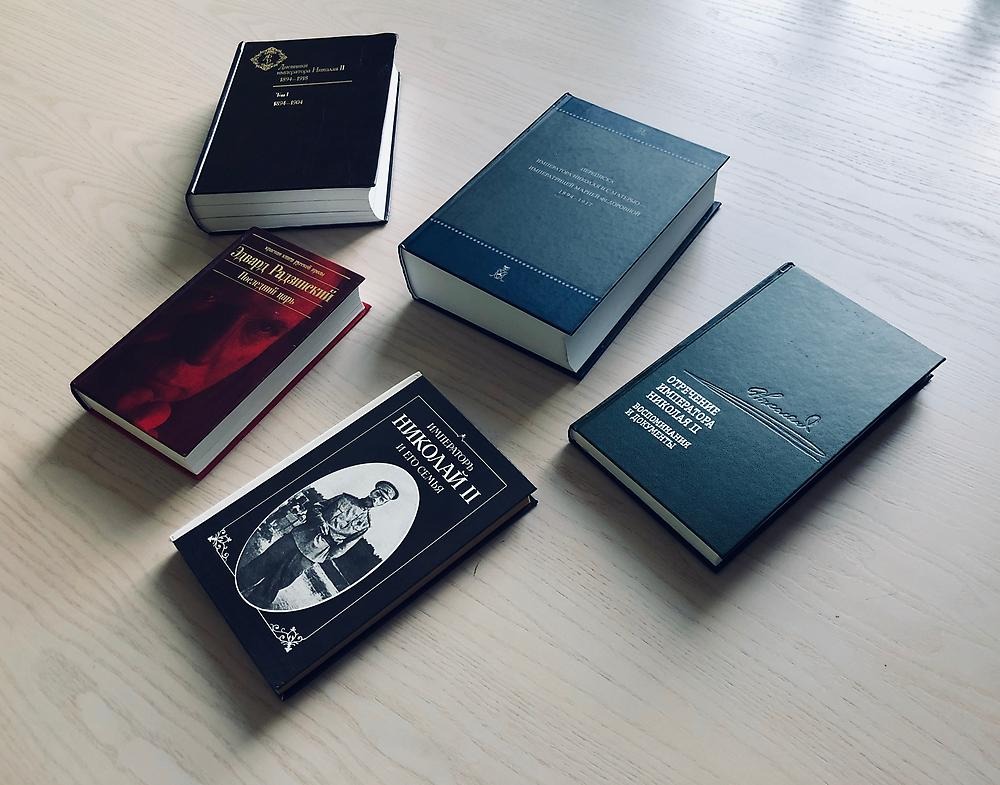 Fem böcker med ryska titlar ligger utspridda på ett träbord. På den främre syns en man i uniform, Nikolaj II.