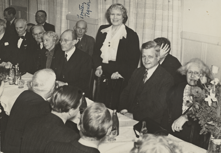 Svartvitt fotografi taget 1945 som visar män och kvinnor runt ett middagsbord. Flera kända antinazister finns med på bilden, bland annat Ture Nerman, Amelie Posse (stående) och Lydia Wahlström (sittande längst till höger).