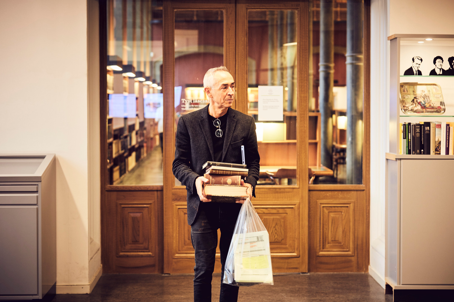 A man standing outside of a large reading room, carrying several books.