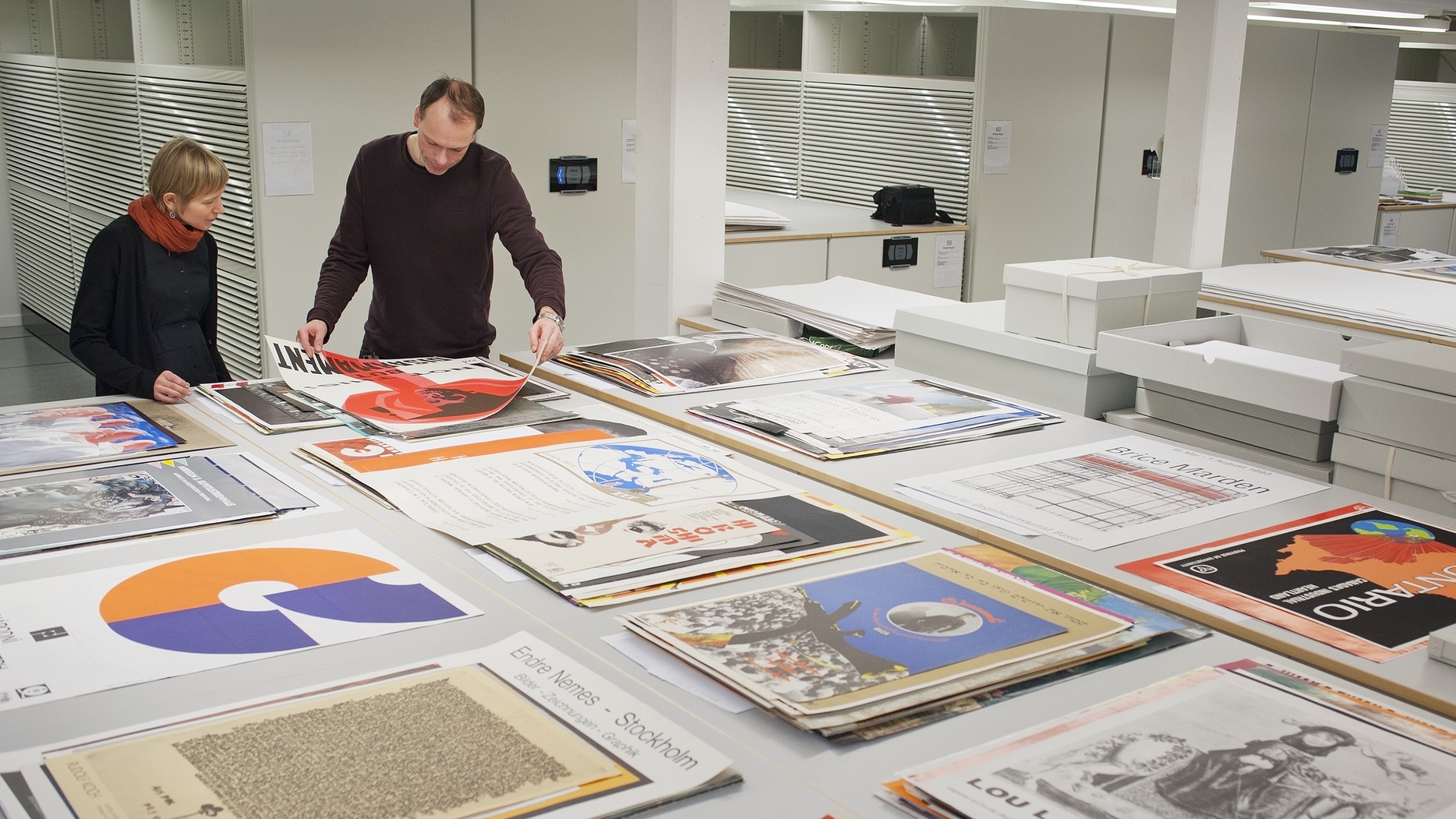 Two persons working with a large number of posters.