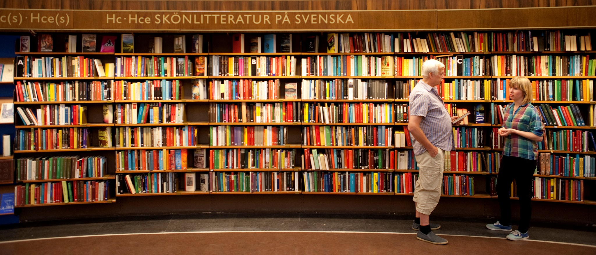 Två personer står vända mot varandra framför en vägg bokhyllor.