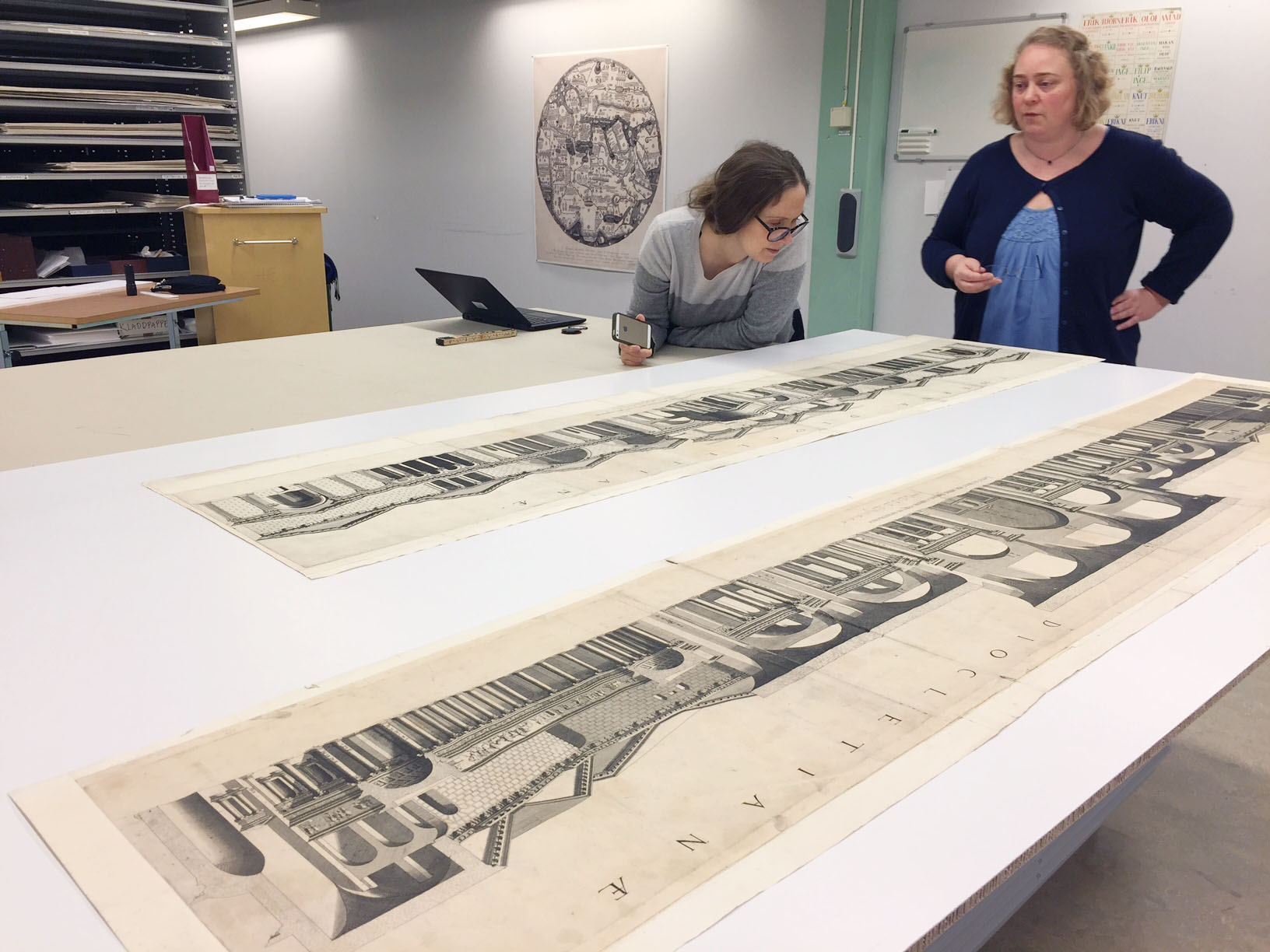En konservator och en bibliotekarie tittar på två stora vyer ur samlingen Foto: Jens Östman, KB