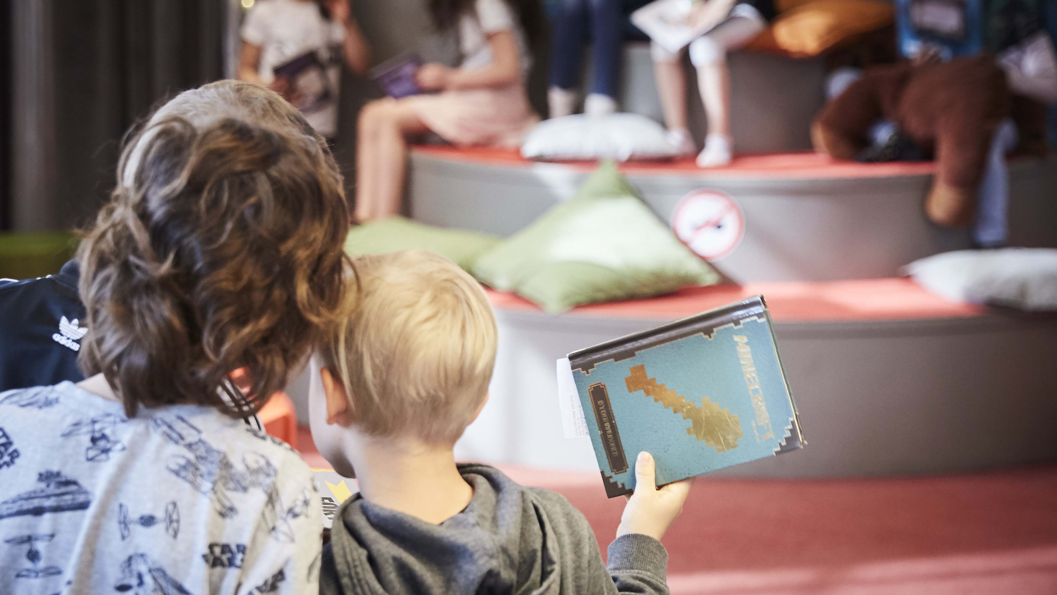 Två barn håller en Minecraft-bok och lutar huvuden ihop.
