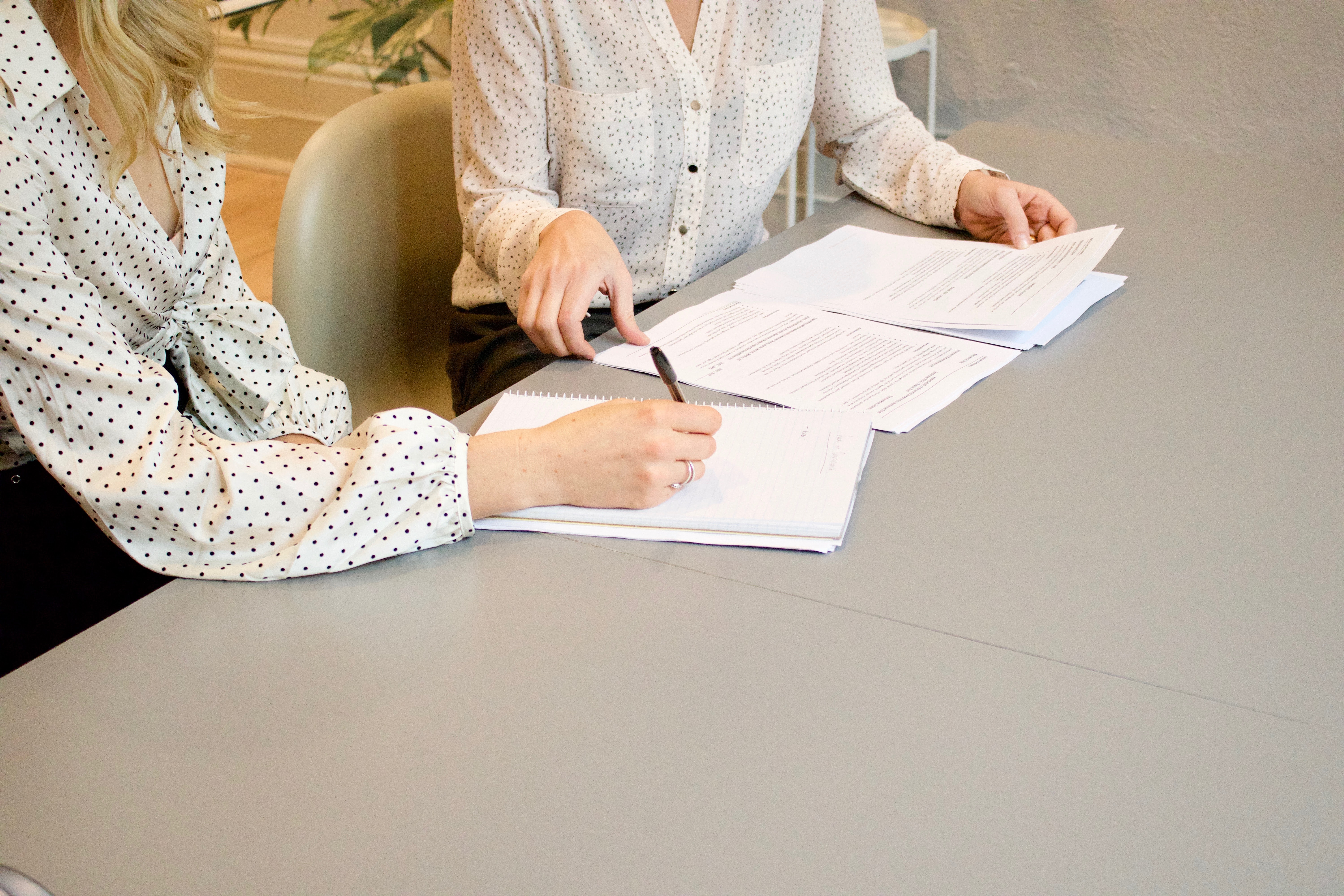 Two persons looking at documents on a table. One of them is writing something.