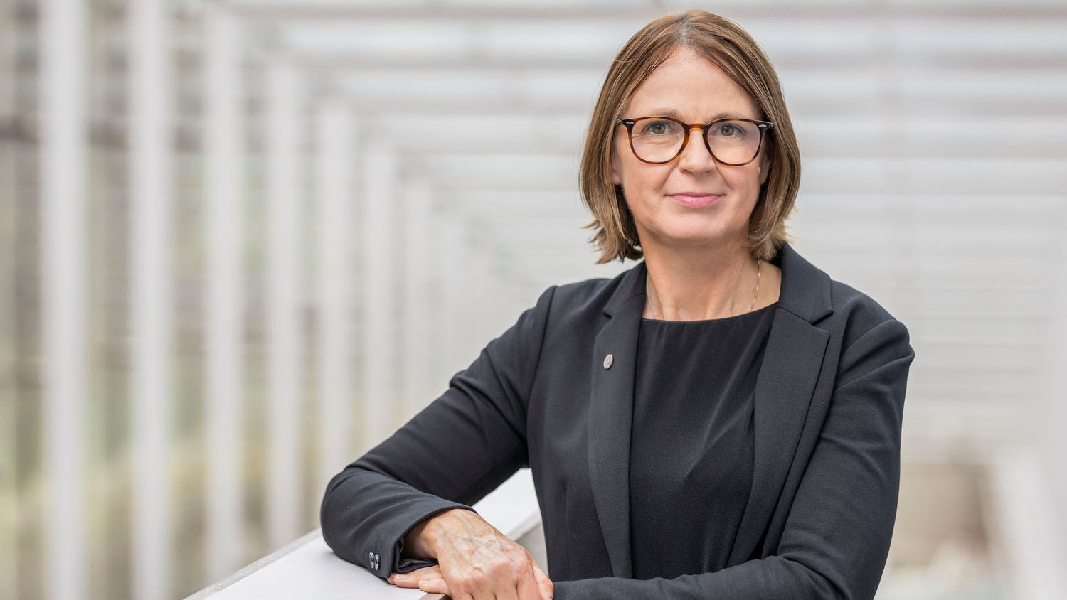 En kvinna med blont hår, glasögon och mörkblå kavaj mot en ljus bakgrund.