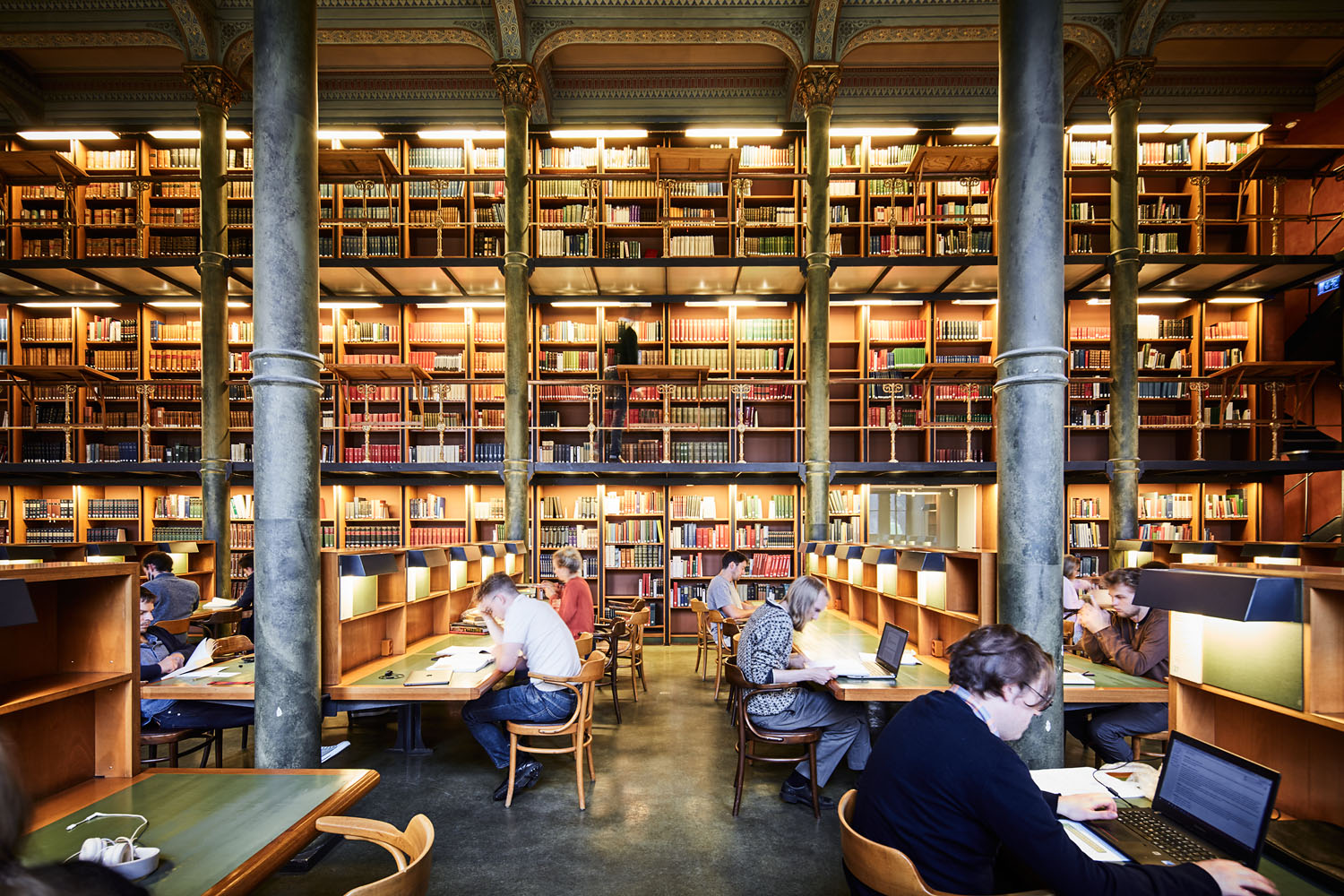 Stor bibliotekslokal i gammal stil med människor som sitter vid bord och studerar.