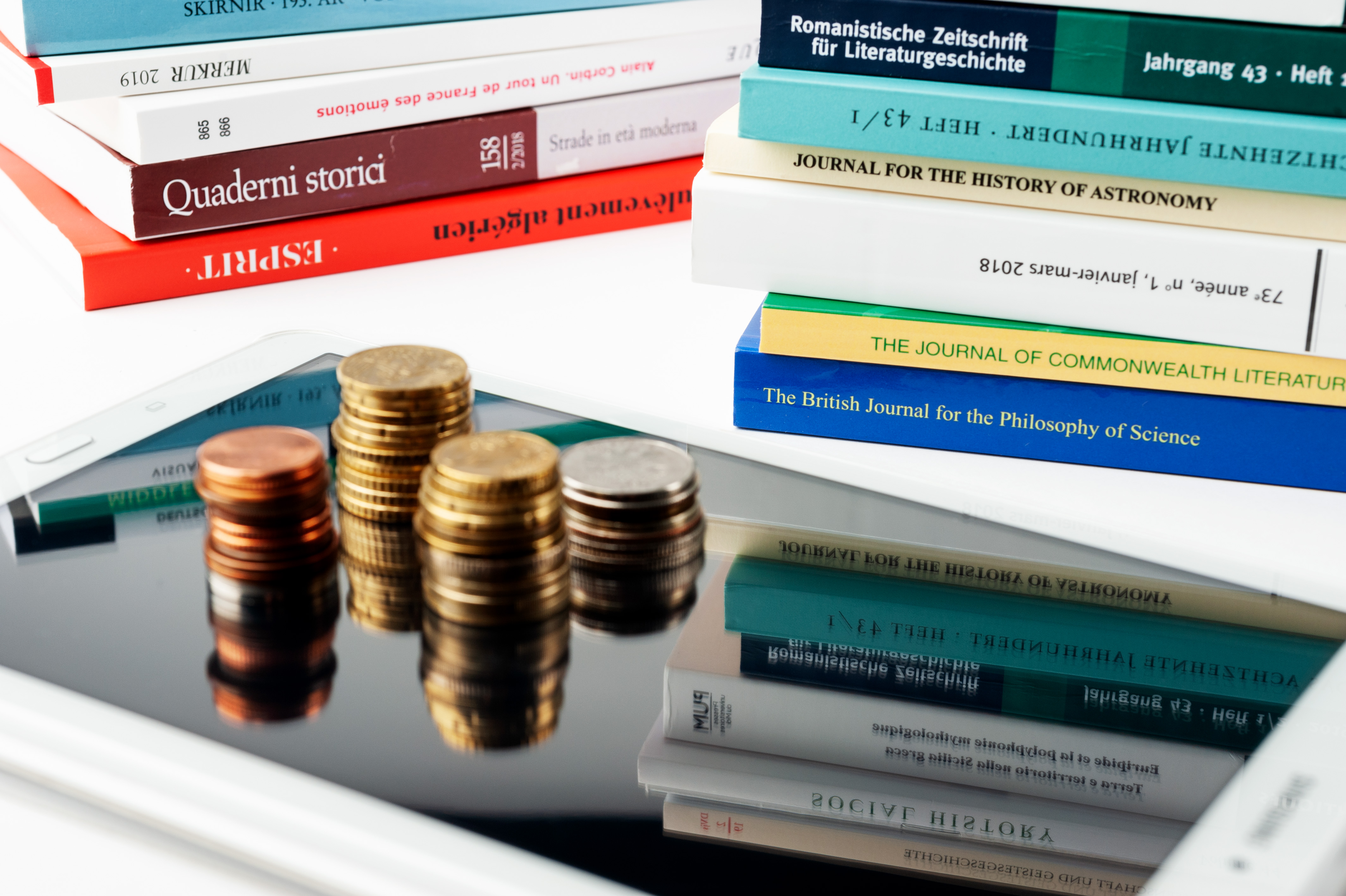 An ipad with coins on top. It is surrounded by scientific books.