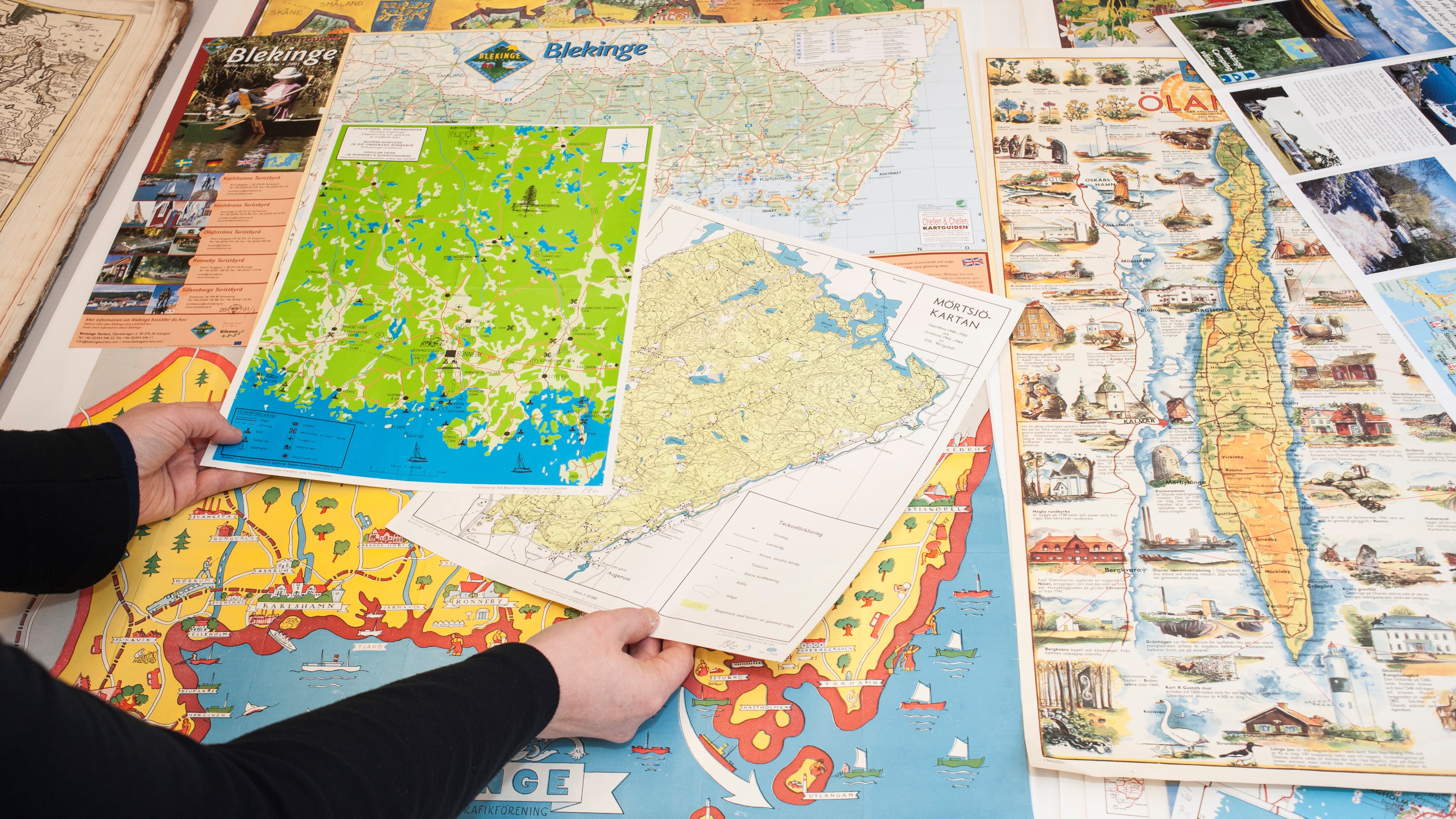 A pair of hands and several maps of different places in Sweden.