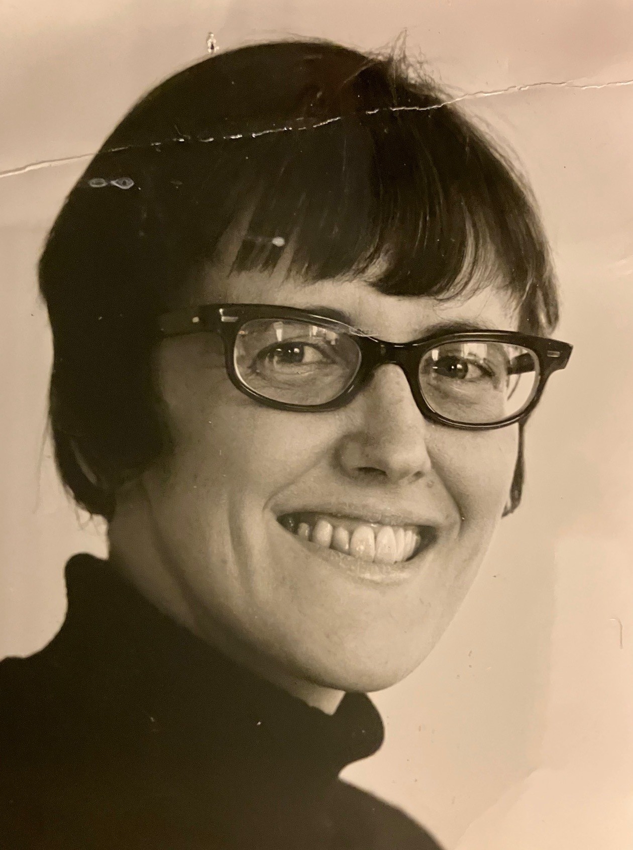 Svartvitt fotografi av leende kvinna med kortklippt, mörkt hår och glasögon.
