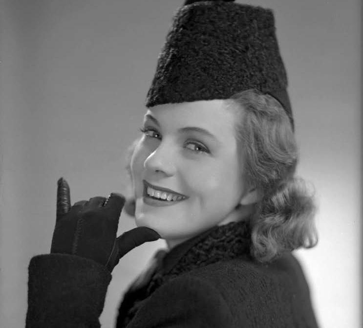 Svartvitt fotografi av leende kvinna i hatt.