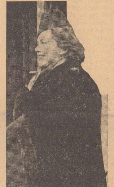 Fotografi ur gammal tidning av leende kvinna med svart kappa och huvudbonad.