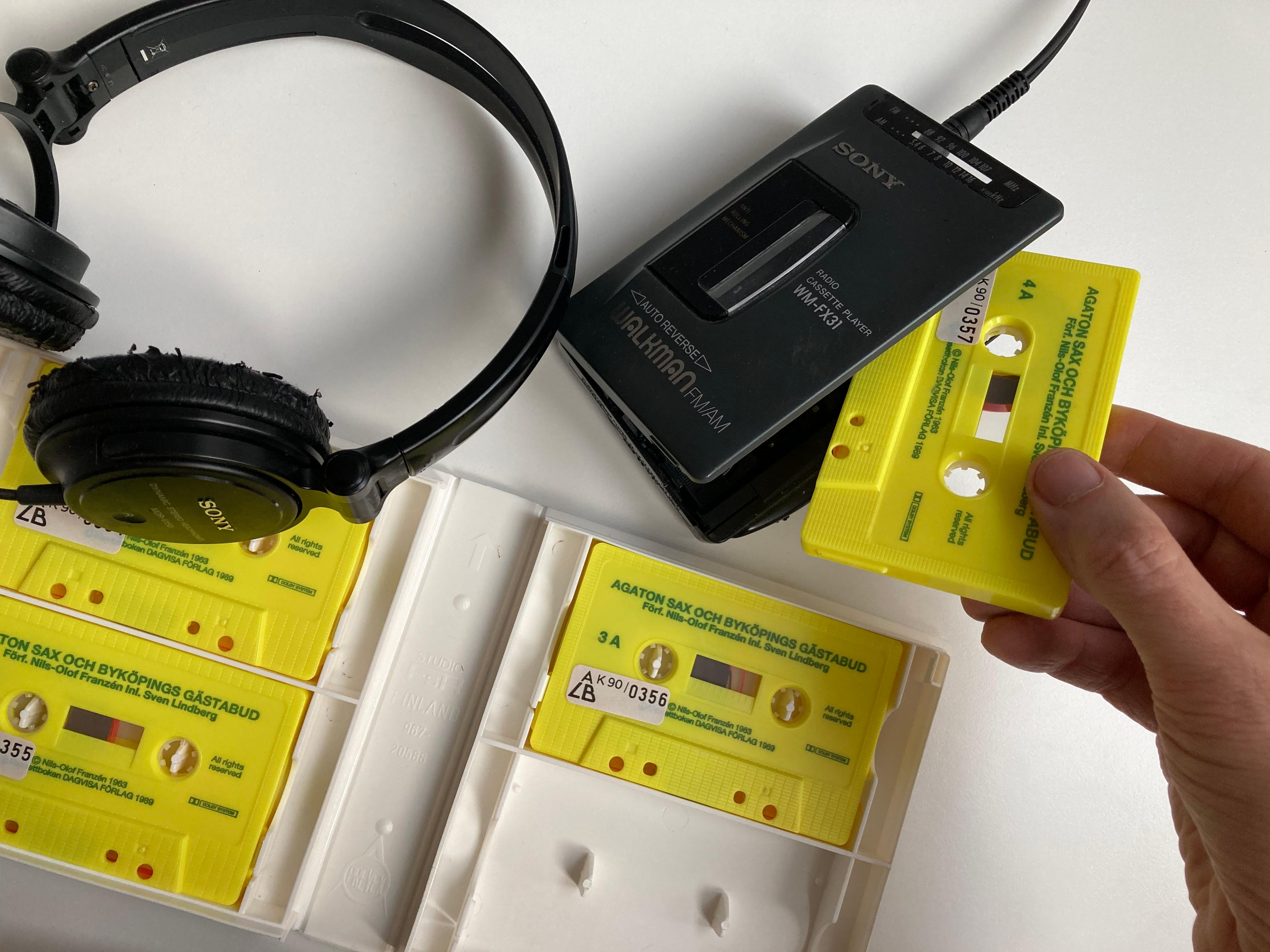 En hand sätter in ett gult kassettband i en bärbar kassettspelare med hörlurar.