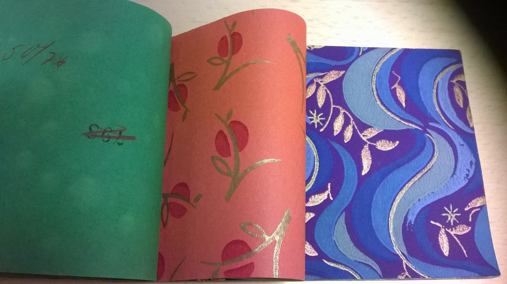 Uppslagen provbok med två mönstrade papper, ett rosa med blommor och ett blått med mönster i silver. 