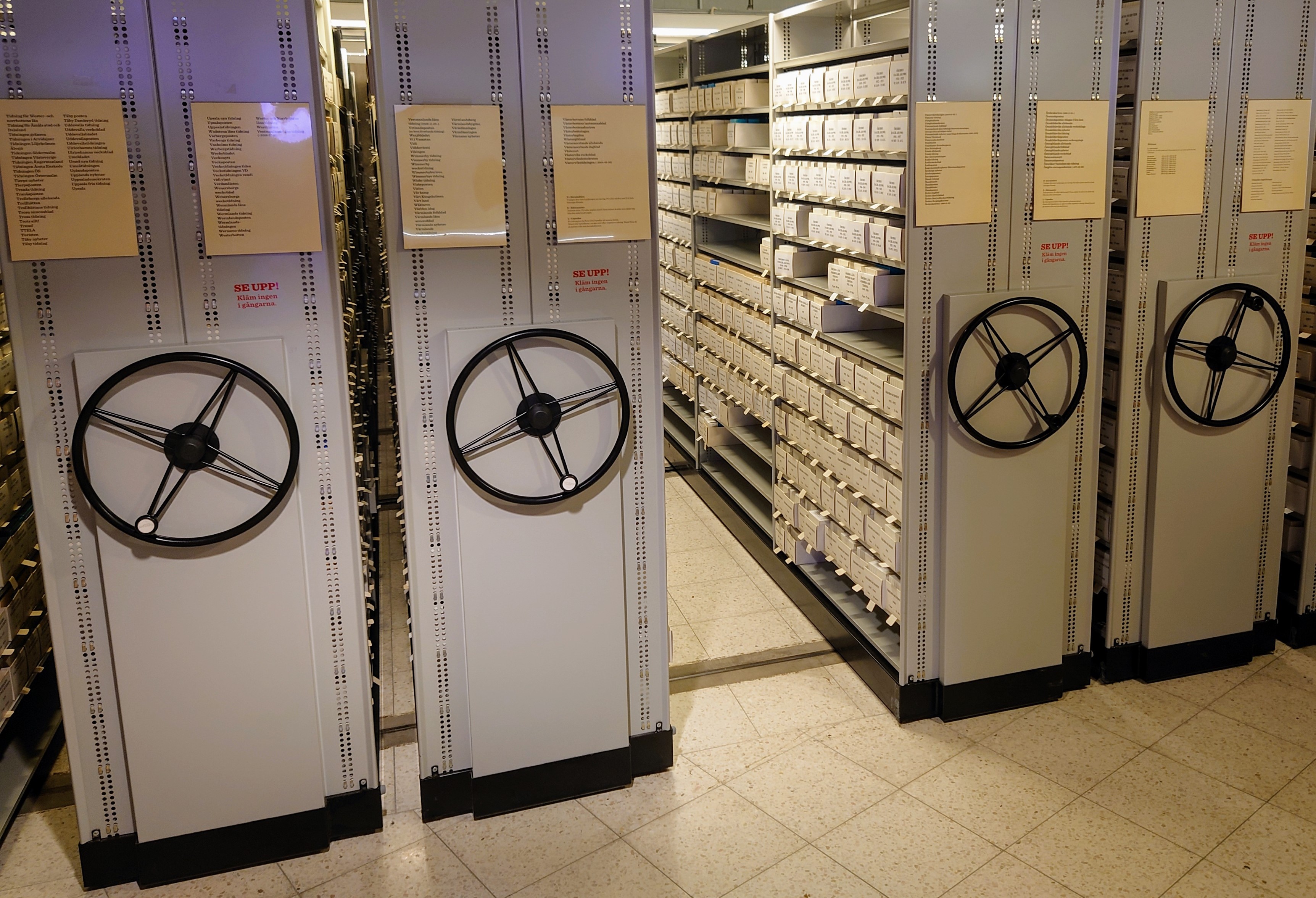 Fotografi på fyra grå kompaktushyllor där vita askar med mikrofilm står uppställda. 