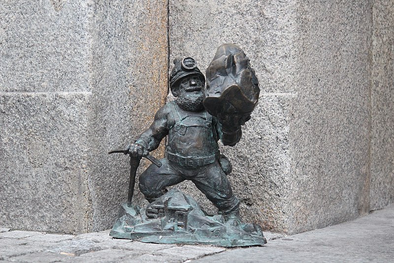 Staty av man som är klädd för gruvarbete, med hjälm, pannlampa och hacka.