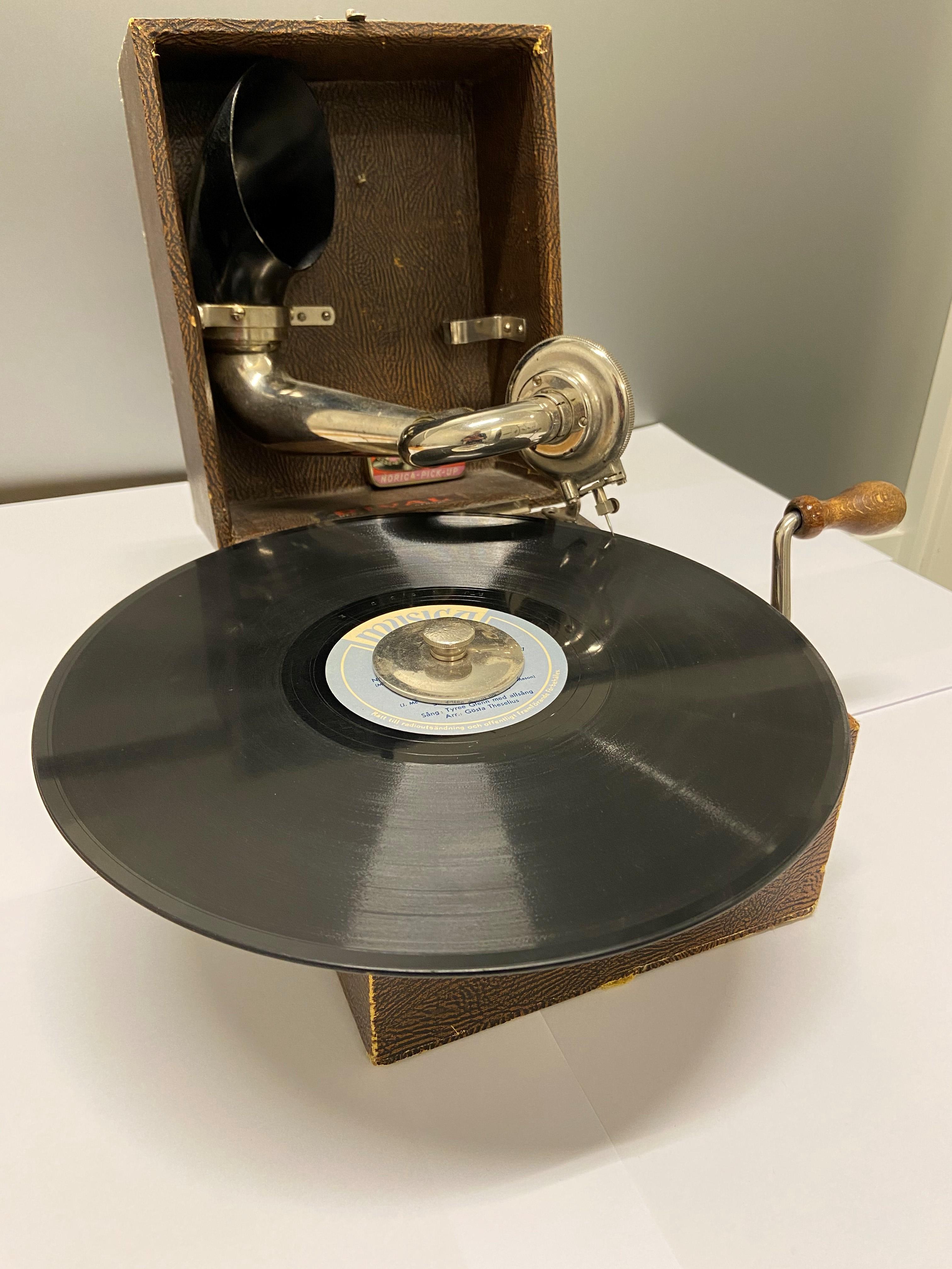 Grammofon i ljusbrun trälåda, med en skiva i centrum.