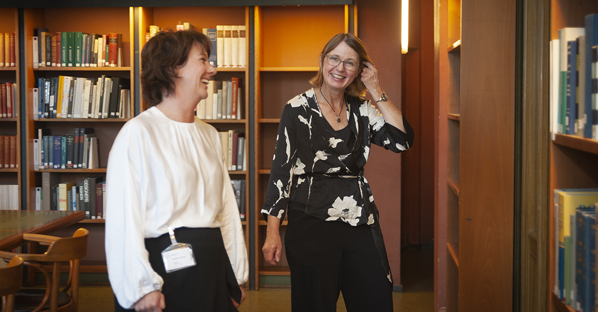 Två skrattande kvinnor pratar med varandra i ett bibliotek.