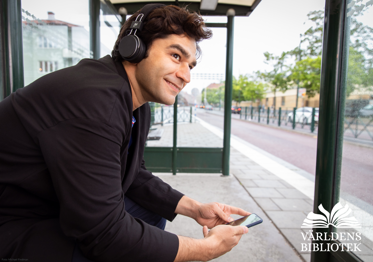 En ung kille sitter på en busshållplats och lyssnar på en bok.