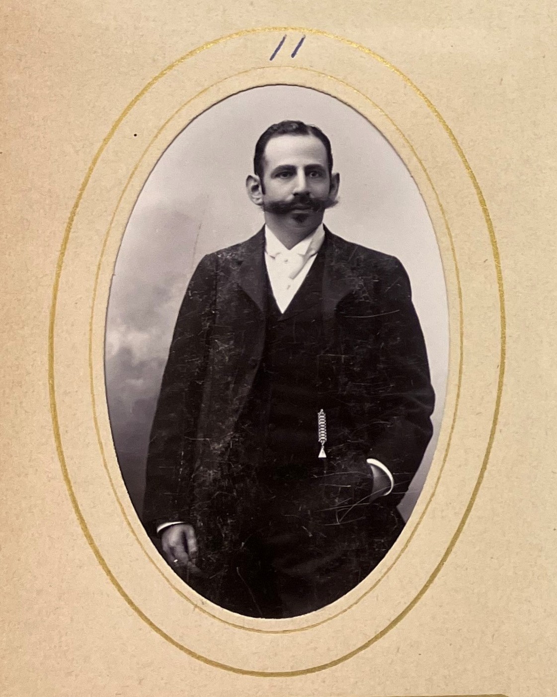 Svartvitt fotografi som föreställer en ung kostymklädd man med mörkt hår och stor mustasch