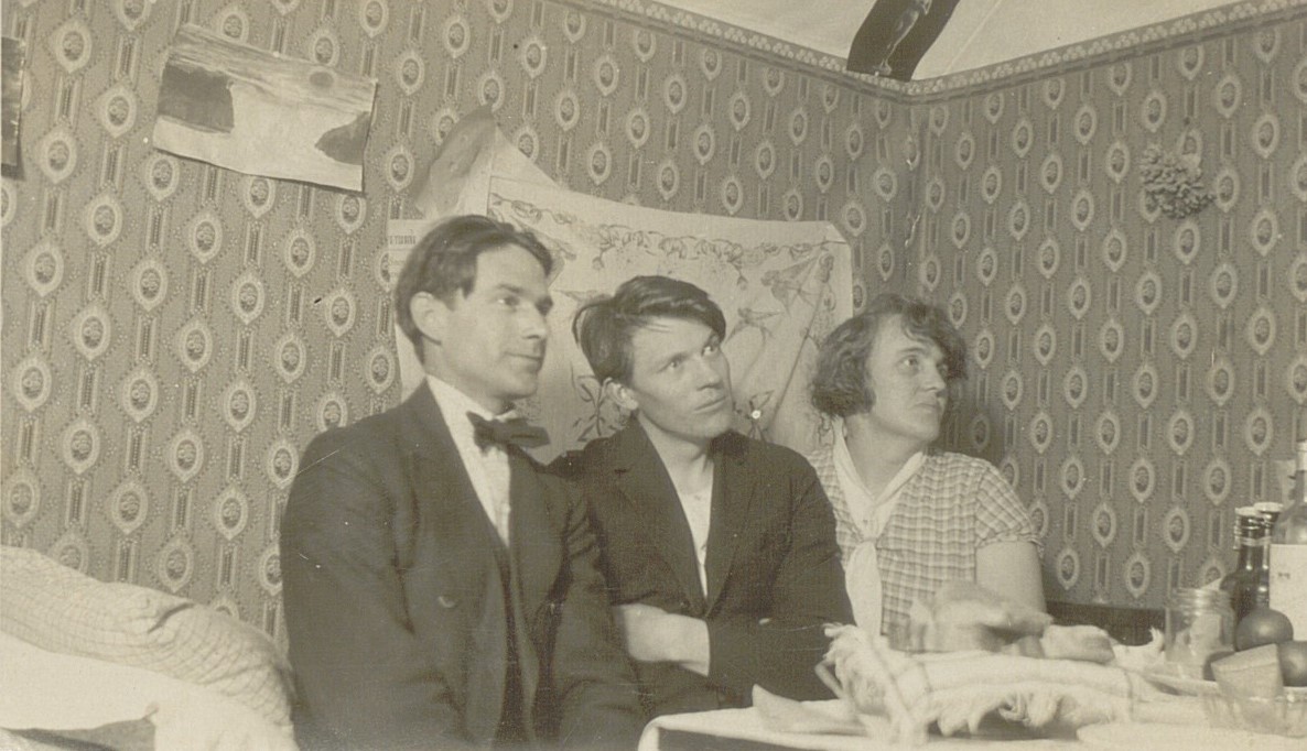 Svartvitt fotografi med två kostymklädda män och en kvinna i klänning.