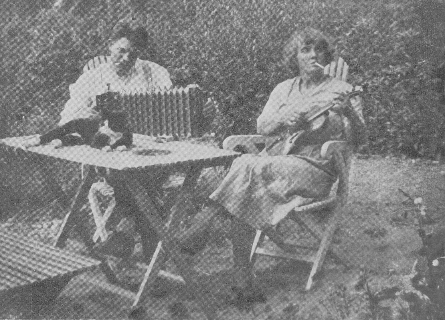 Svartvitt fotografi, mannen på stolen röker och spelar dragspel medan kvinnan också röker och spelar gitarr.