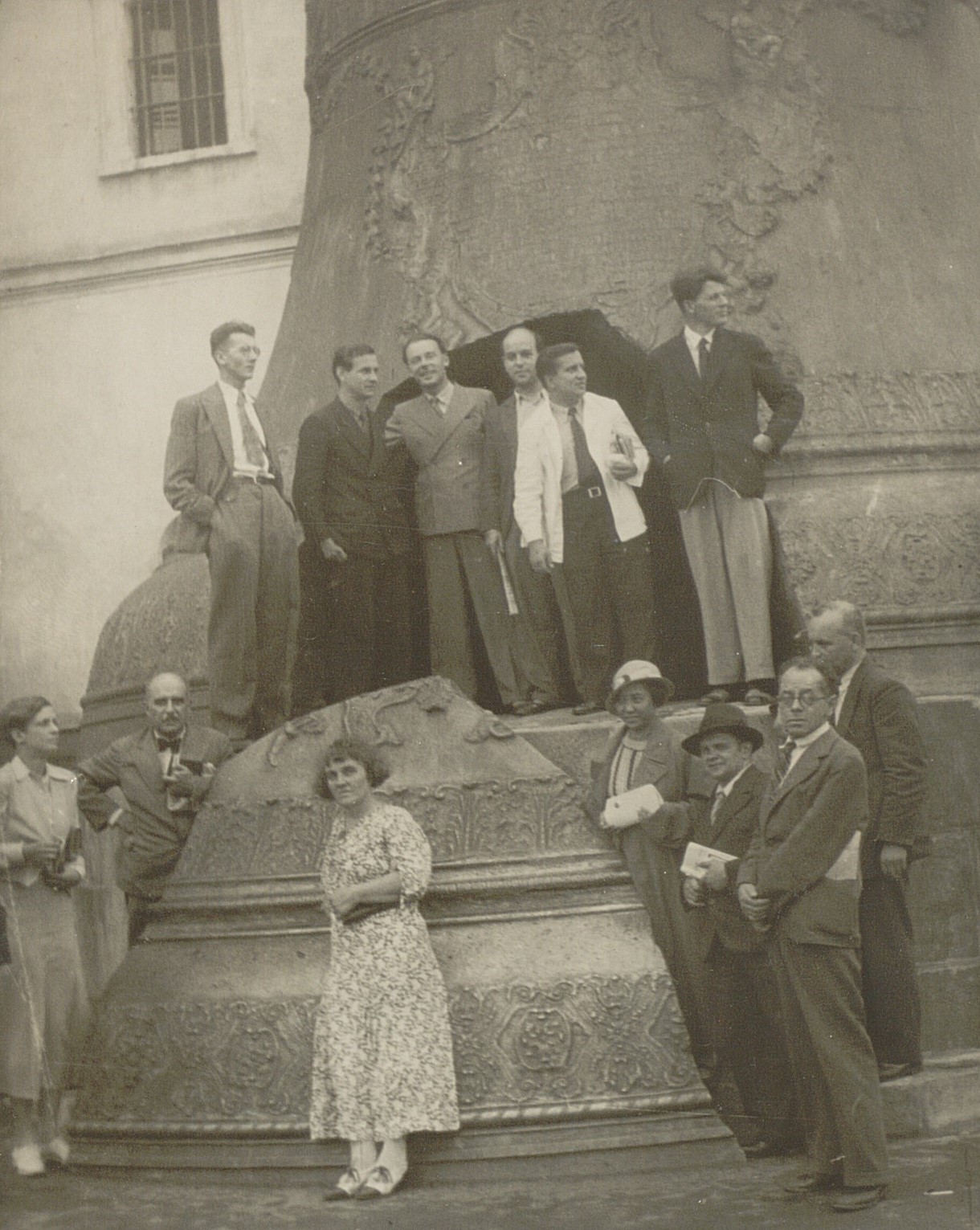 Svartvitt fotografi på sällskap av män och kvinnor framför och uppe på en stor sprucken kyrkklocka.