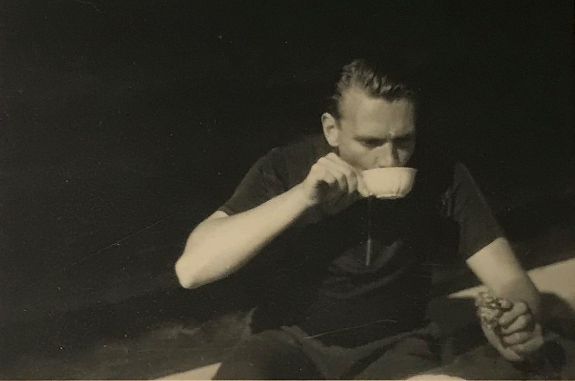 Svartvitt fotografi av en ung man som dricker en kopp kaffe i solen.