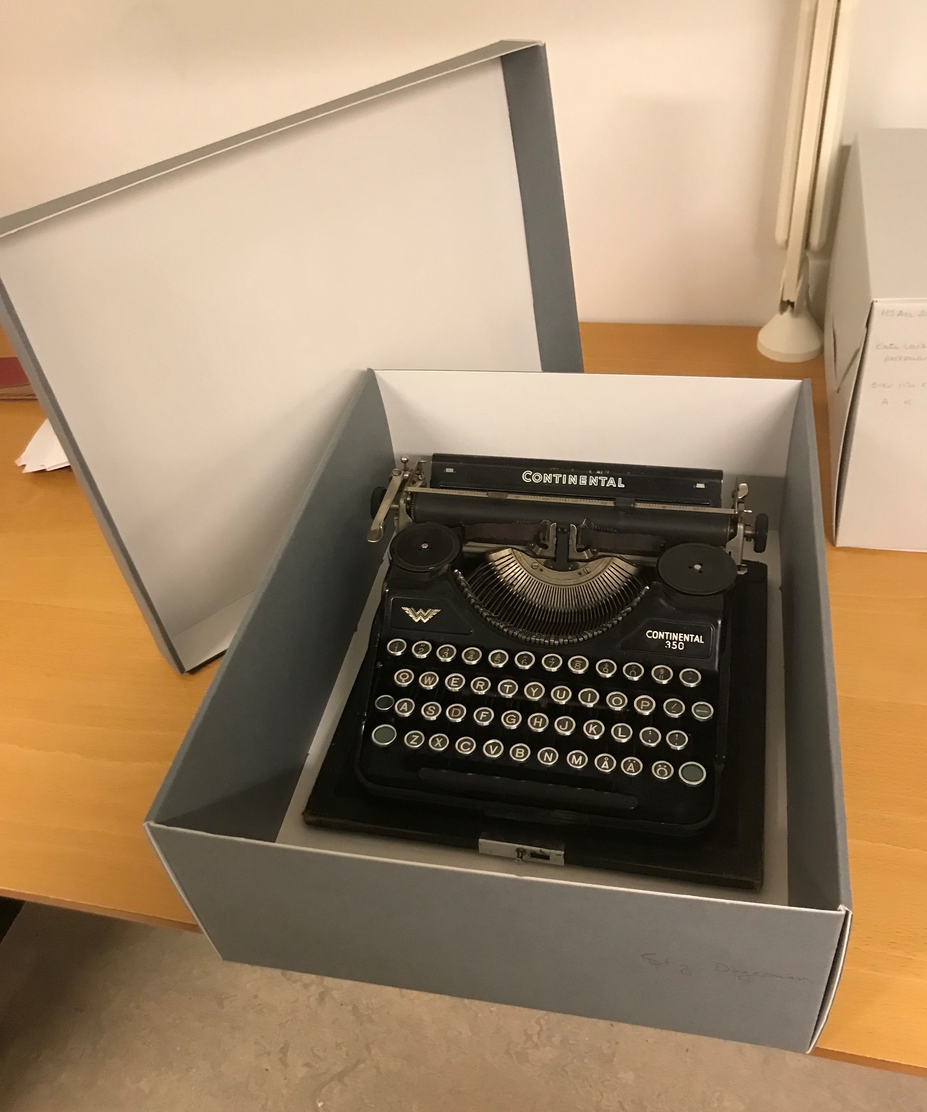 Färgfotografi av en gammal svart skrivmaskin som förvaras i en grå arkivkartong.