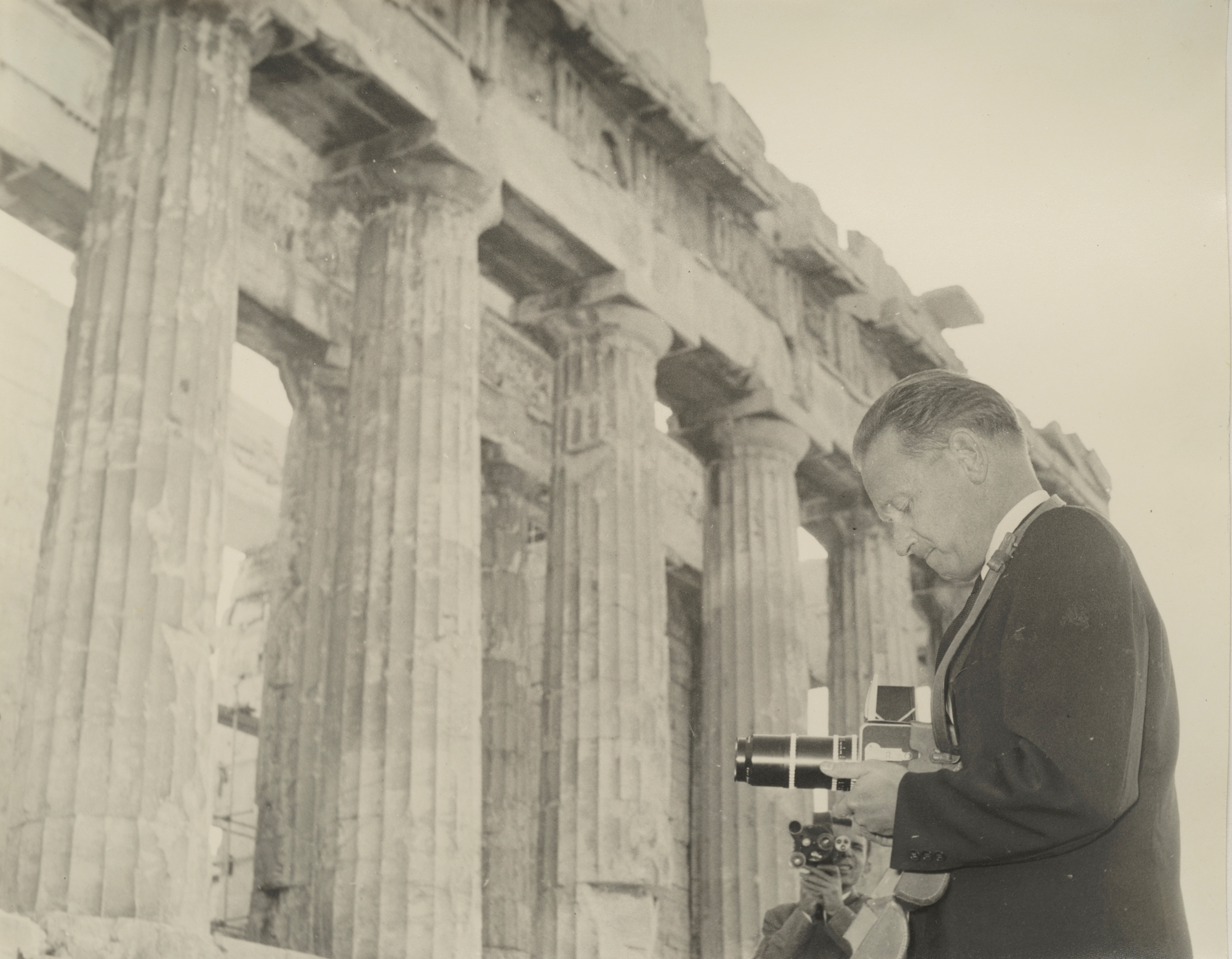 En man med en kamera står nedanför en antik byggnadsruin med höga pelare