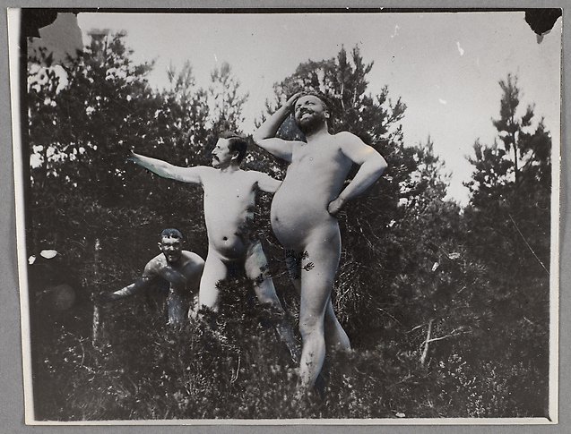Svartvitt fotografi av tre nakna män som ser lekfulla ut i naturen.
