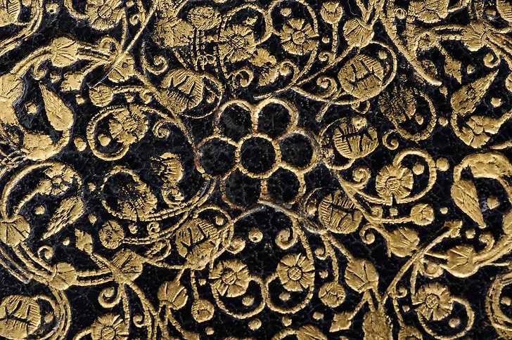 Närbild av äldre bokband i svart läder med blomornament i guld.